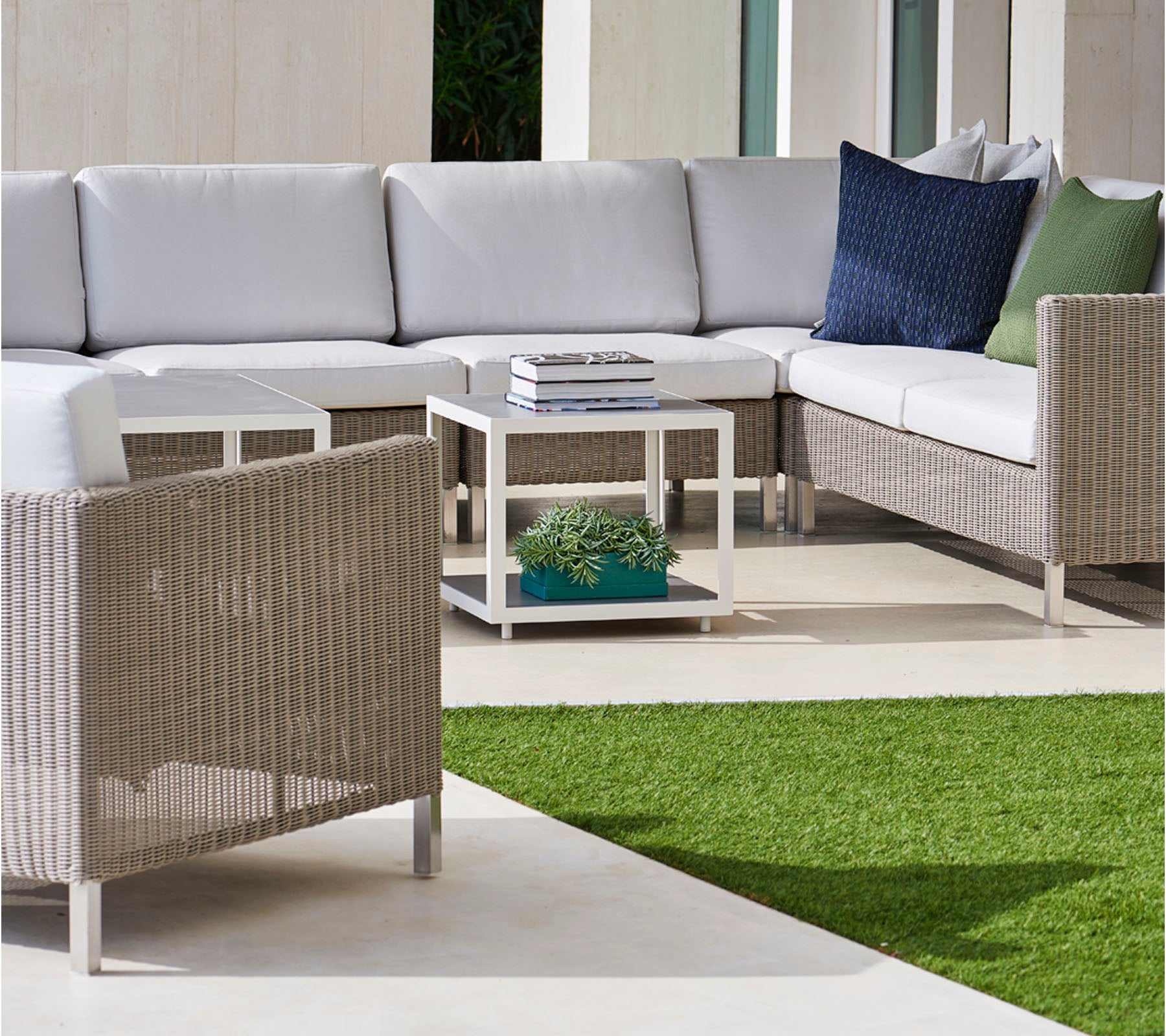 Stilvolles Außenbereich mit einer Ecksofa mit grauen Kissen, gemütlichen Kissen und einem modernen Couchtisch auf einer üppigen grünen Fläche.