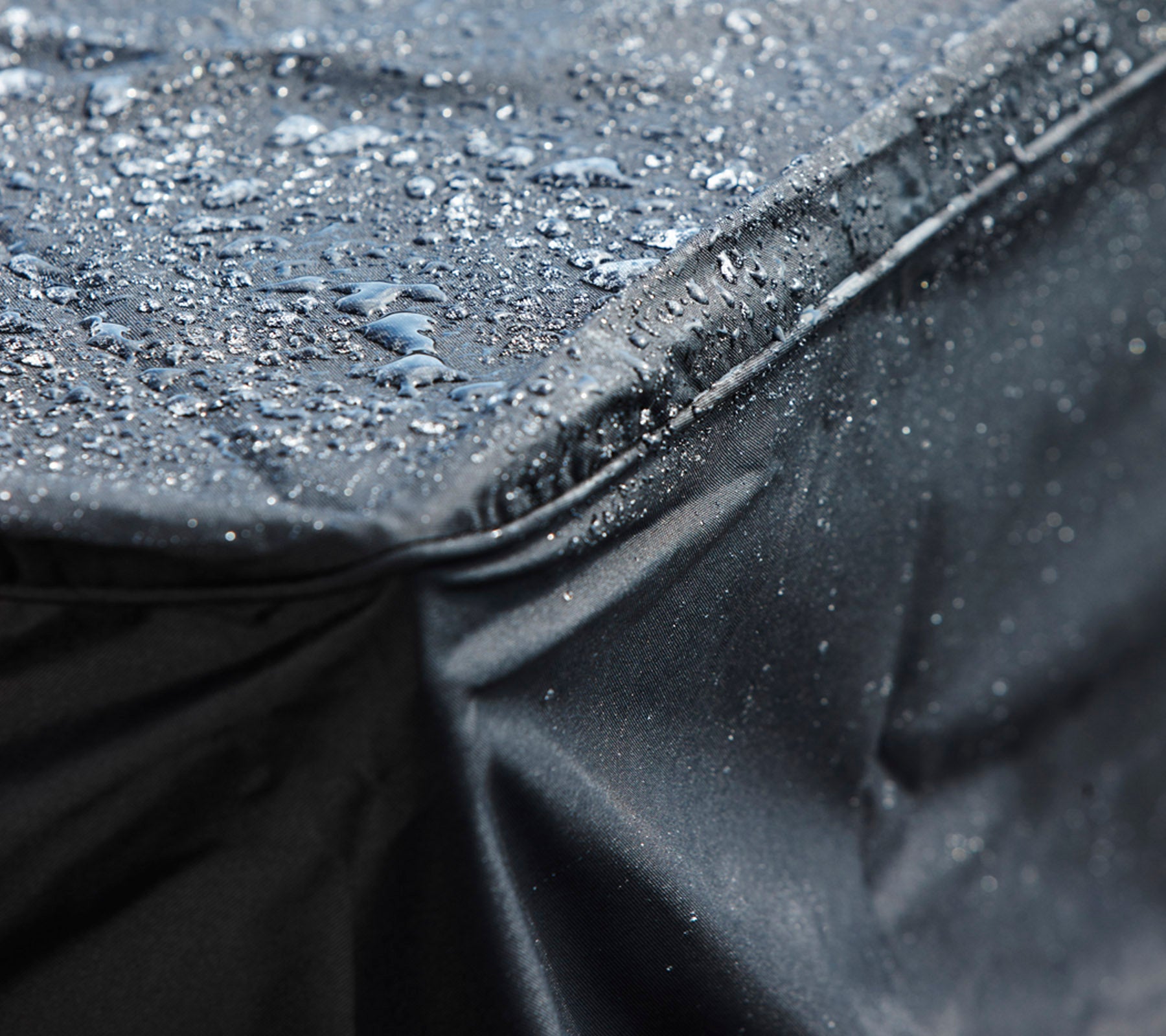 Nahaufnahme einer schwarzen wasserdichten Abdeckung mit Wassertropfen auf der Oberfläche, die ihr schützendes Design zeigt.