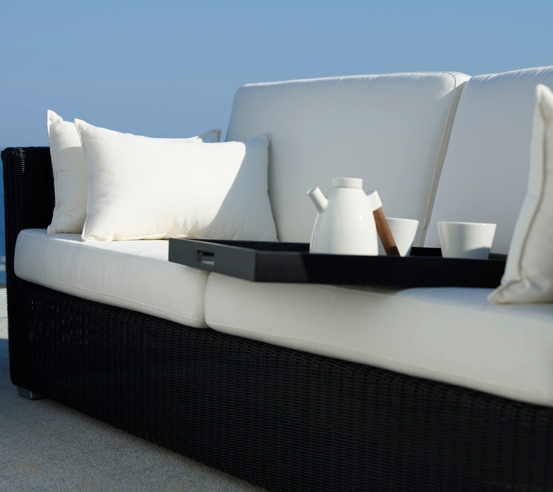 Stylische Couch mit weißen Kissen und einem schwarzen Rahmen, ausgestattet mit einem Tablett, einer Teekanne und Tassen für eine gemütliche Atmosphäre.