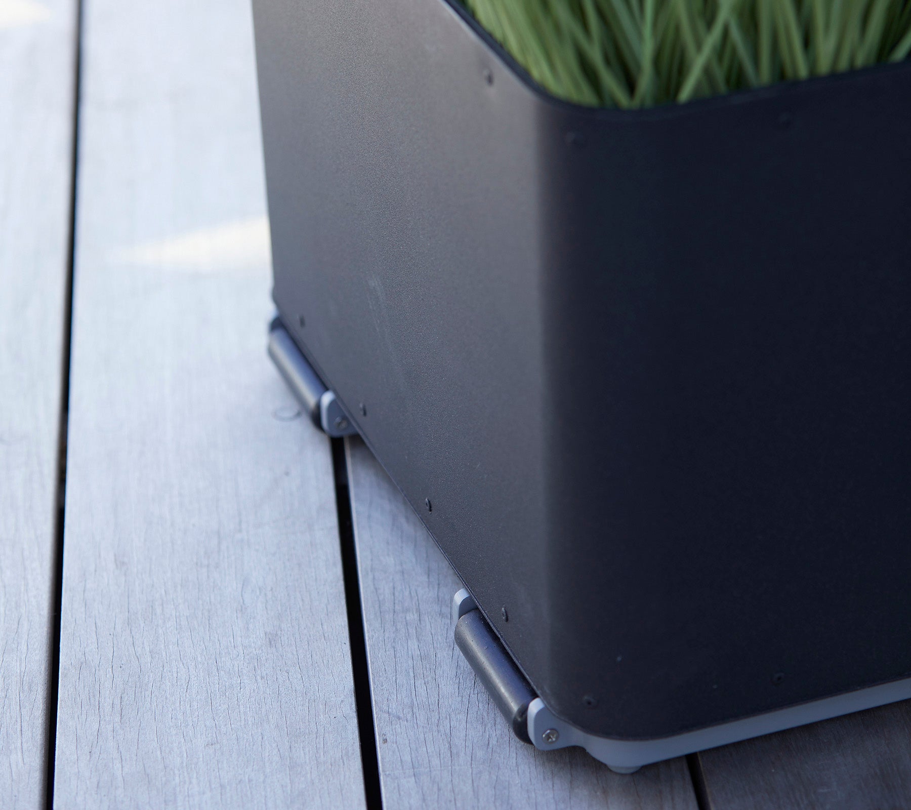 Schwarze Pflanzbox mit sleekem Design, featuring grünem Gras und silbernen Verbindern auf einer Holzoberfläche.