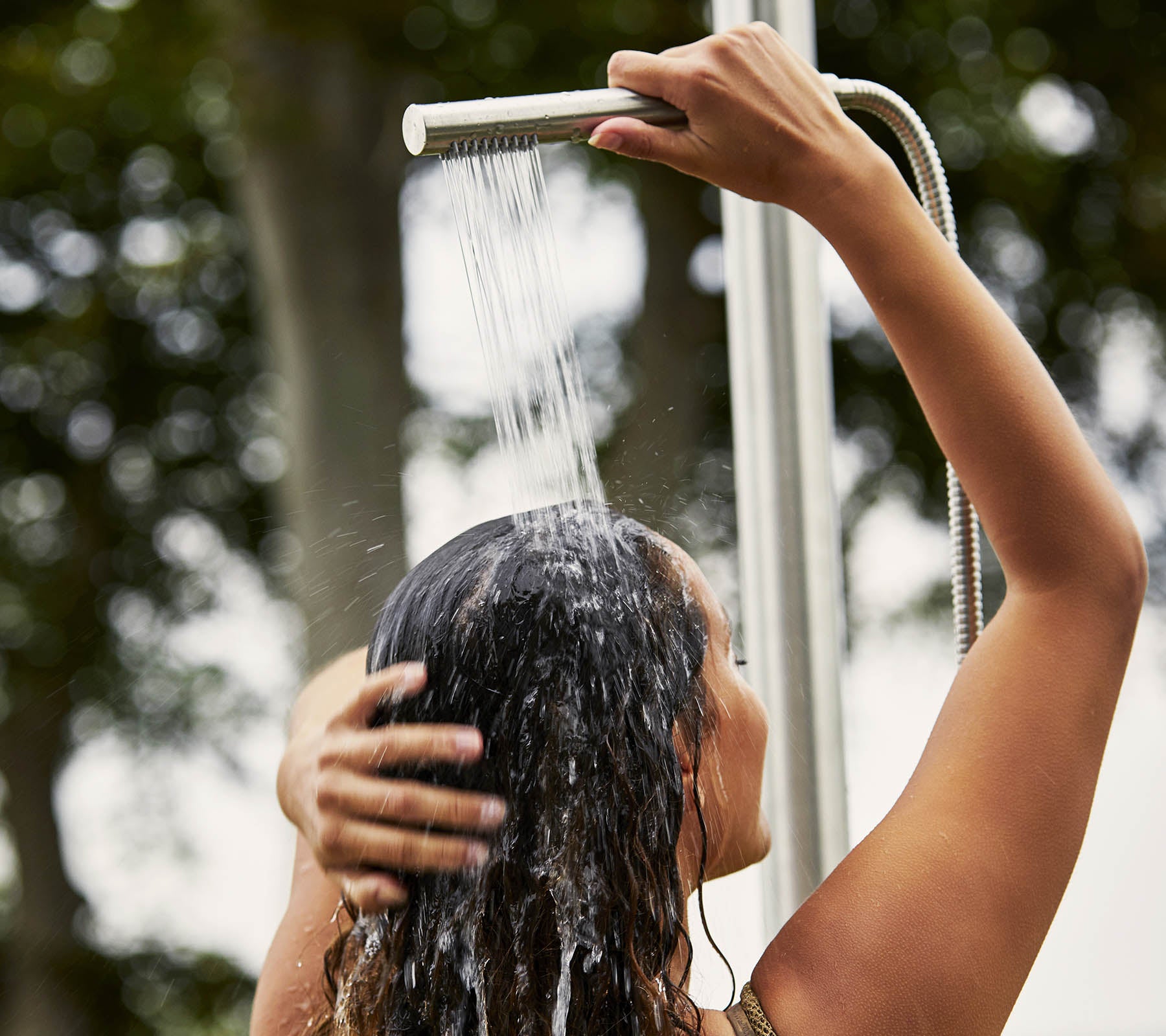 Eine Person, die sich unter der Dusche die Haare wäscht, während das Wasser herabfließt und sie von einer natürlichen Umgebung umgeben ist.