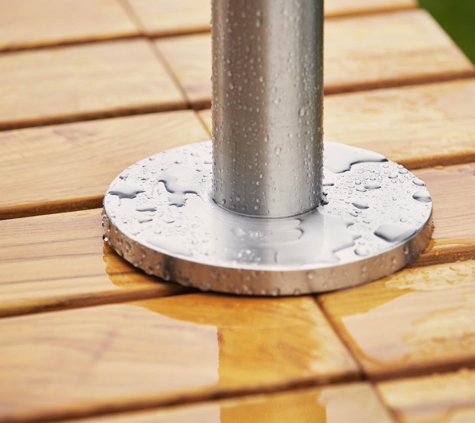 Metallbasis mit einem Pfosten, der auf einer Holzoberfläche ruht, mit Wassertropfen auf sowohl der Basis als auch dem Holz.