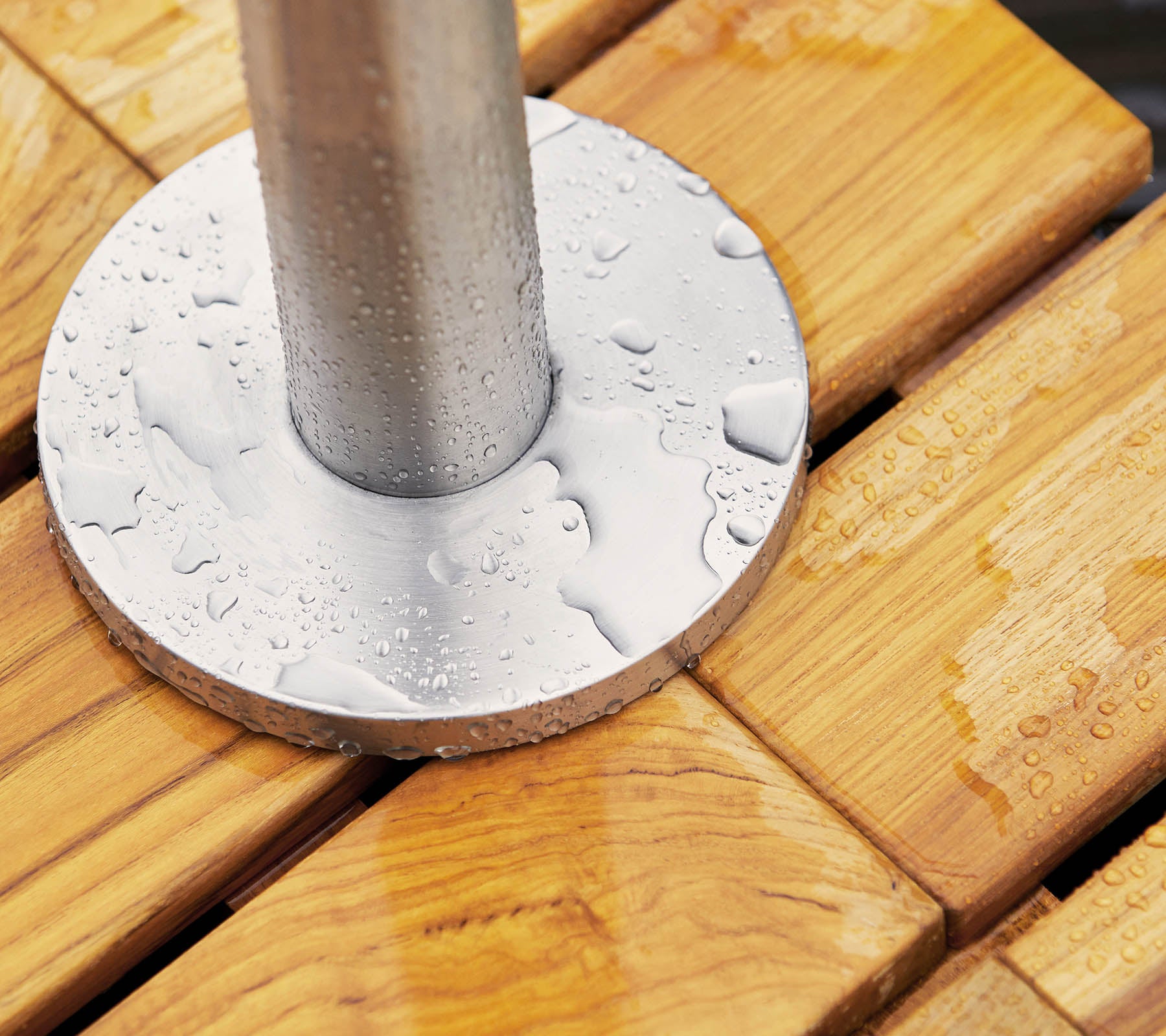 Metallbasis mit Wassertropfen, die auf einer Holzoberfläche ruhen, mit glatten, lamellenartigen Planken und einem zylindrischen Pfosten in der Mitte.