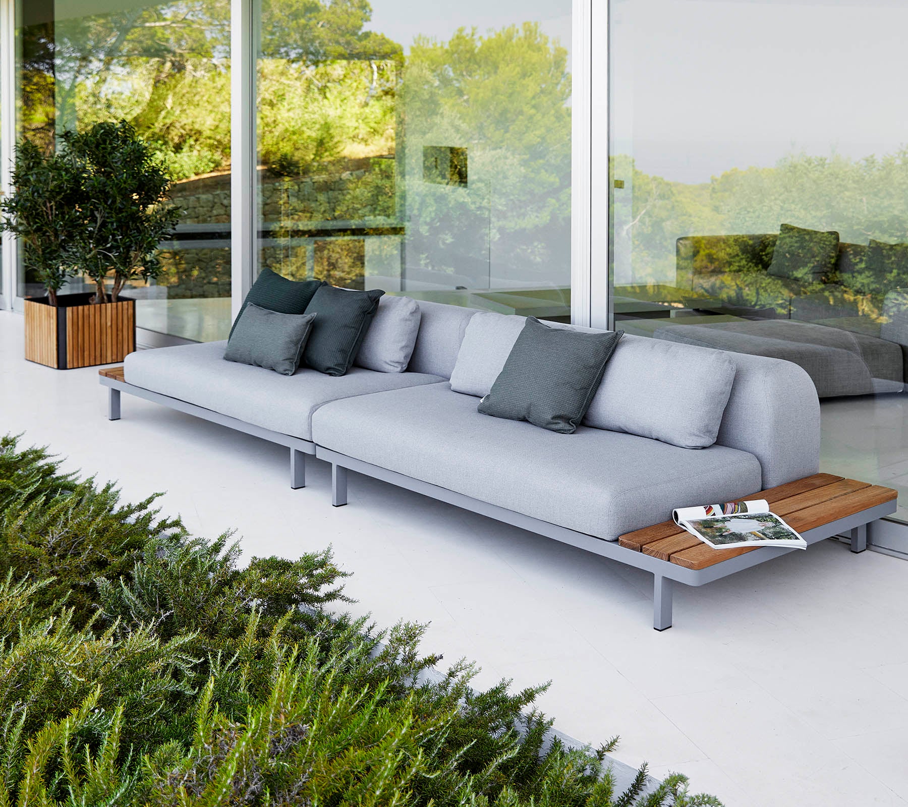 Moderne Sofa mit hellgrauen Kissen und Holzakzenten, begleitet von dekorativen Kissen und umgeben von Grünpflanzen.