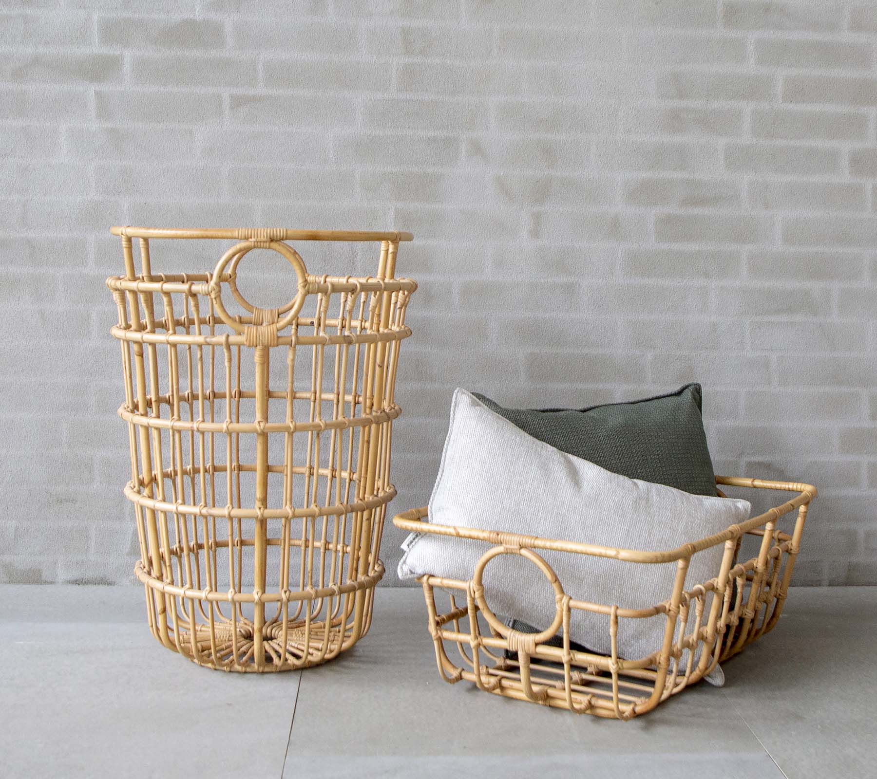 Moderne geflochtene Körbe mit grauen und grünen Kissen in einem minimalistischen Setting.