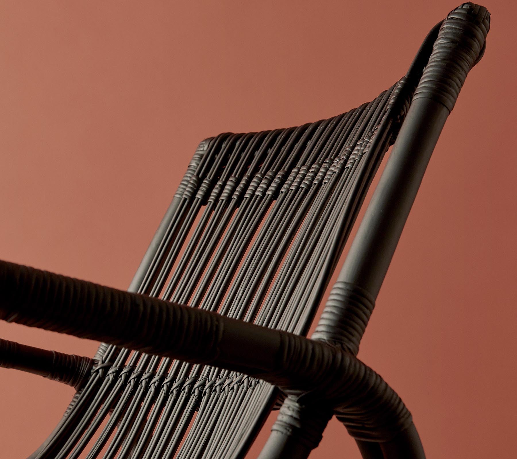 Eine Nahaufnahme einer geflochtenen Stuhllehne vor einem warmfarbigen Hintergrund, die ihr komplexes Design und ihre Textur hervorhebt.