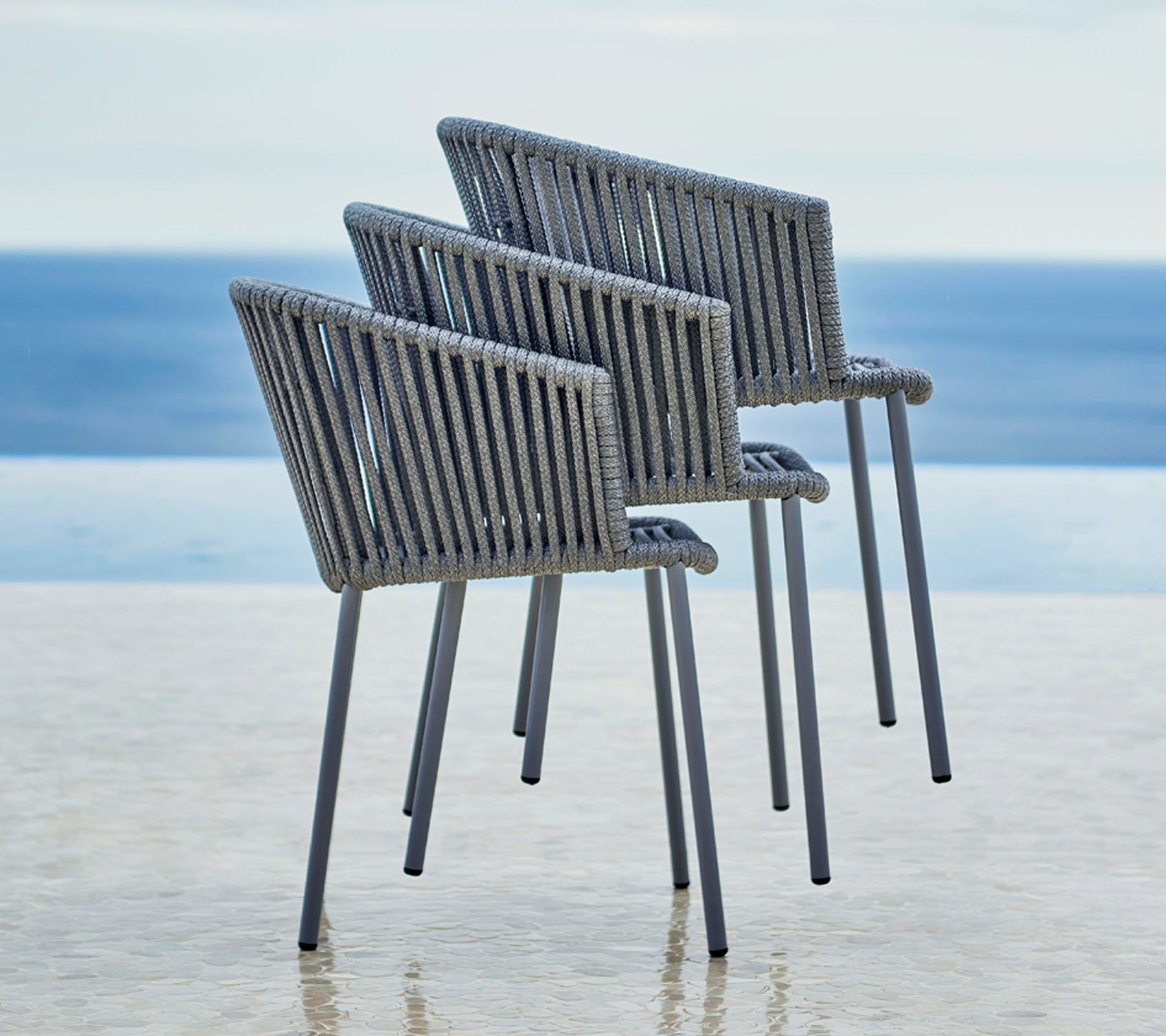 Drei moderne Stühle mit einem stilvollen Design, ausgestattet mit einem Lattenrücken und Armlehnen, positioniert neben einem ruhigen Wasserblick.