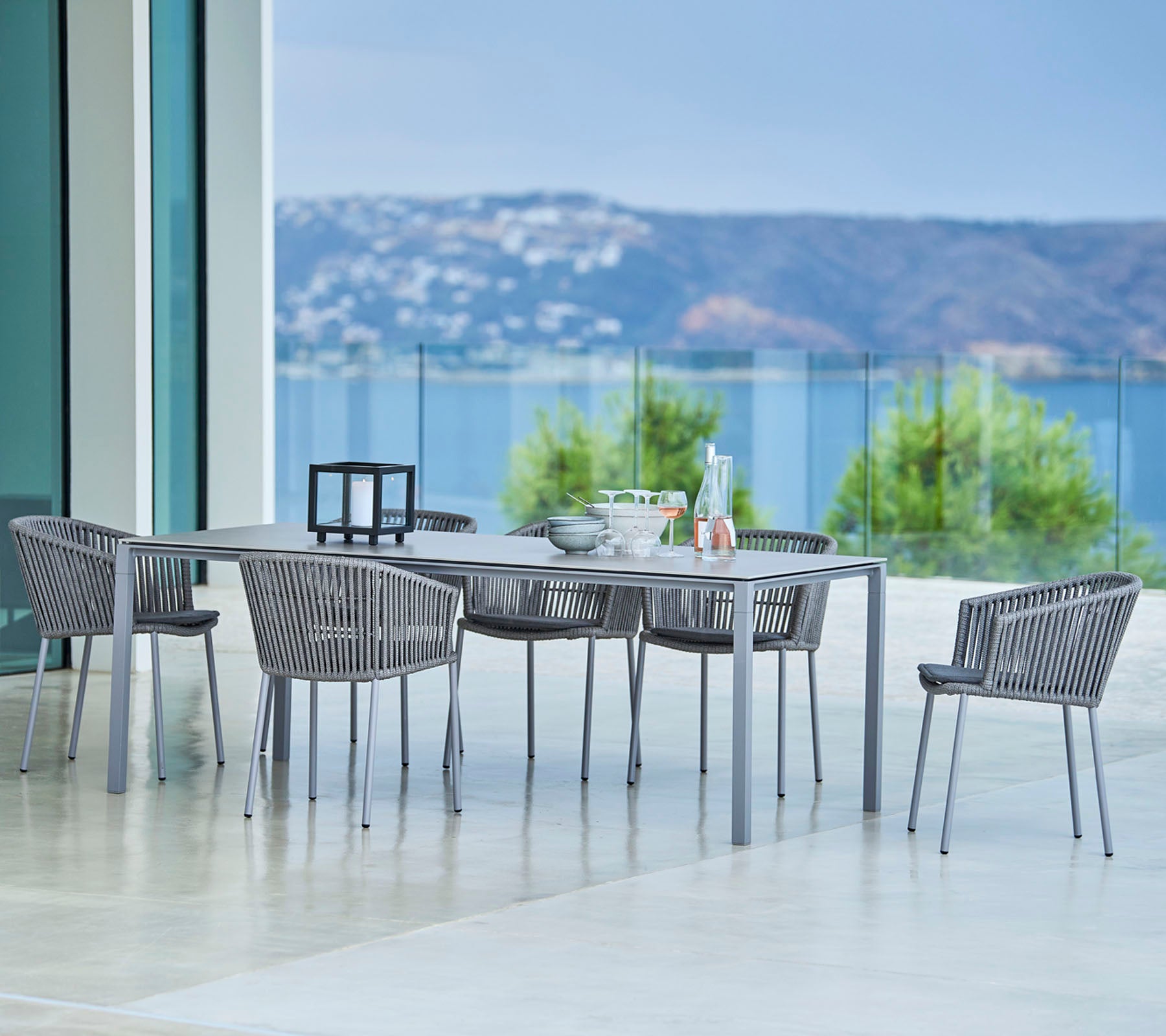 Elegantes Essgruppe für den Außenbereich mit einem rechteckigen Tisch und stilvollen geflochtenen Stühlen mit malerischem Blick im Hintergrund.