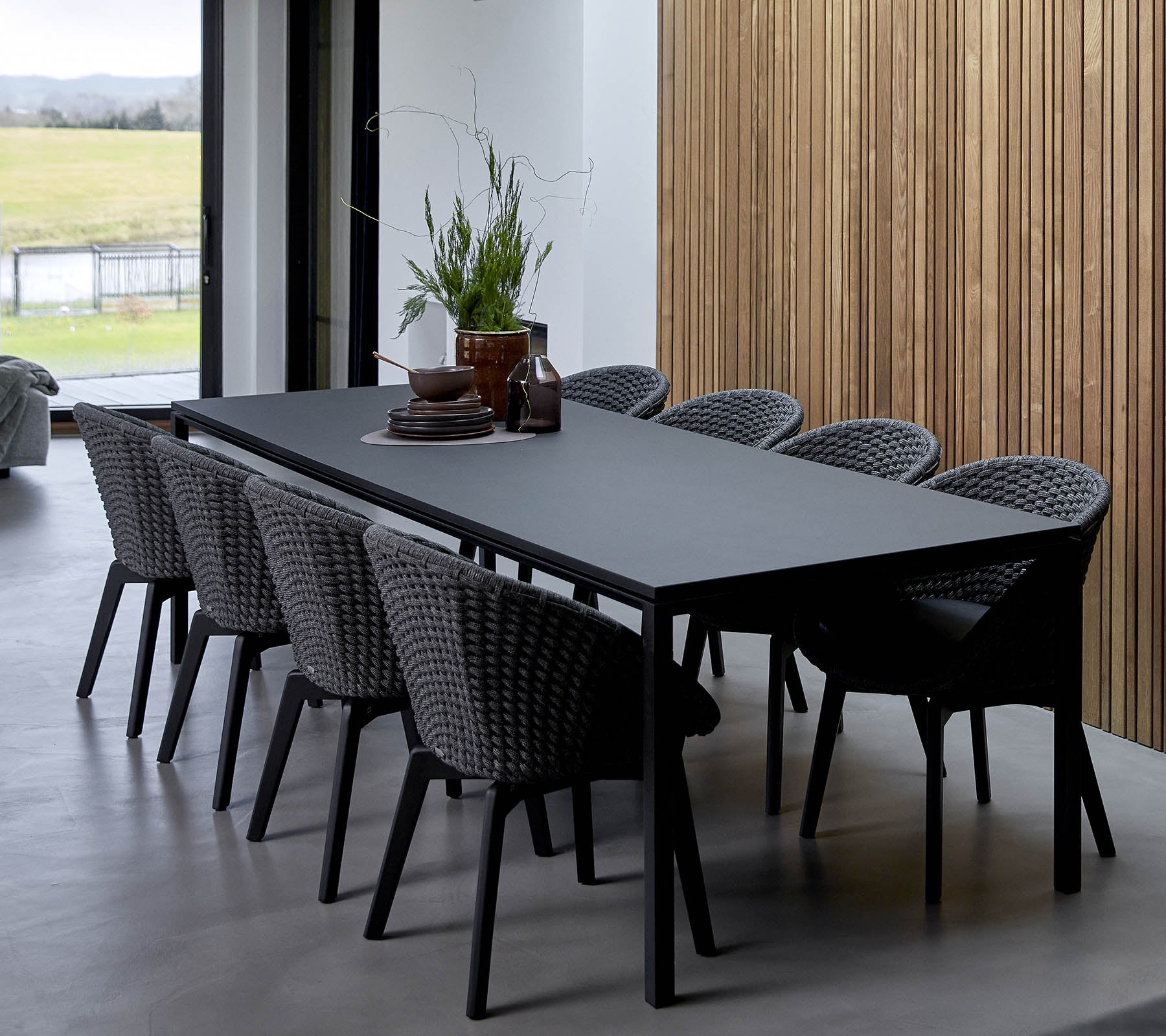 Ein eleganter Tisch umgeben von geflochtenen Stühlen, geschmückt mit dekorativen Pflanzen und einem Mittelpunkt, vor einem Holz-Hintergrund.