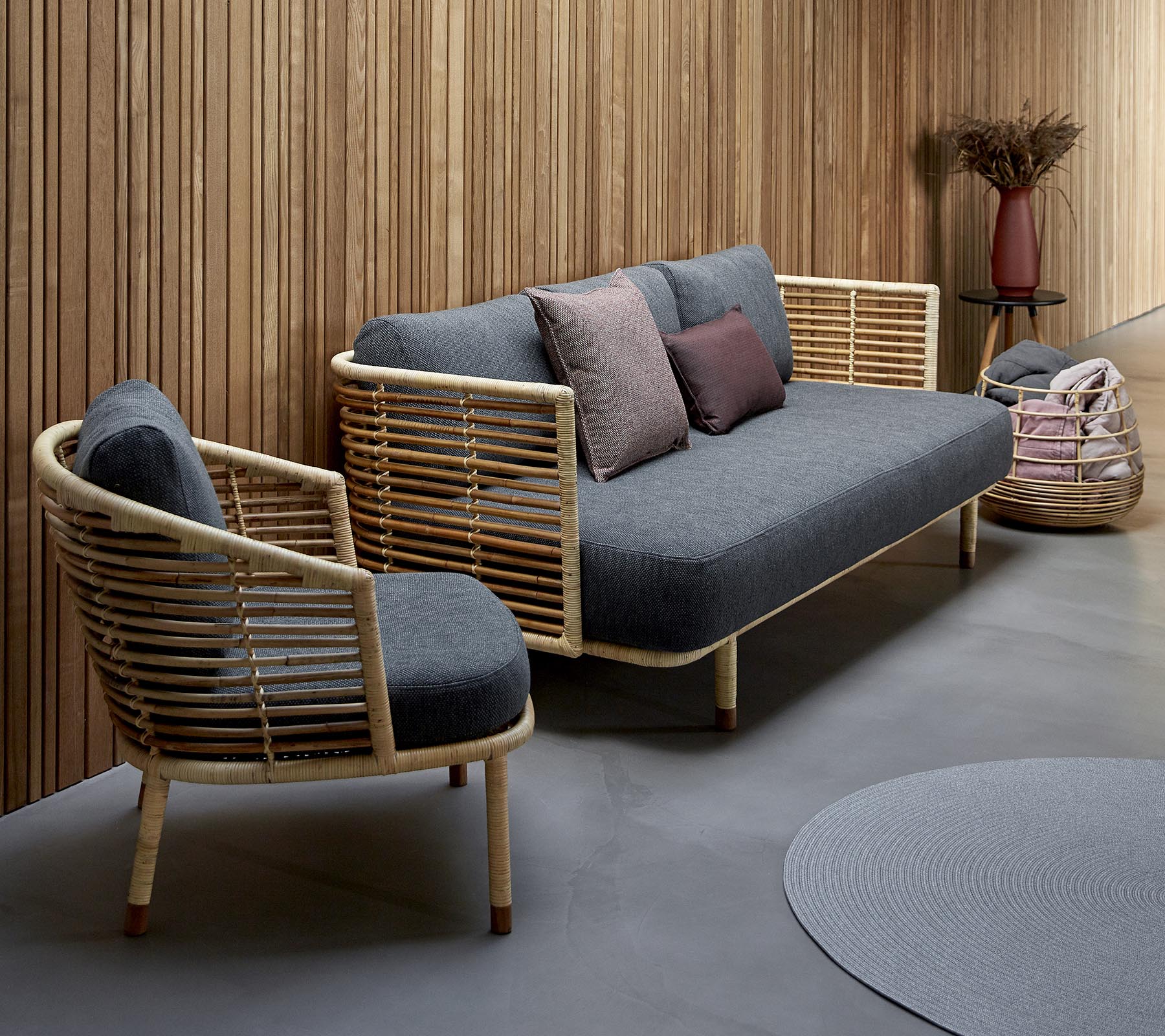 Stilvolles Sitzarrangement mit einem grau gepolsterten Sofa mit Holzakzenten und einem passenden Stuhl, ergänzt durch dekorative Kissen.