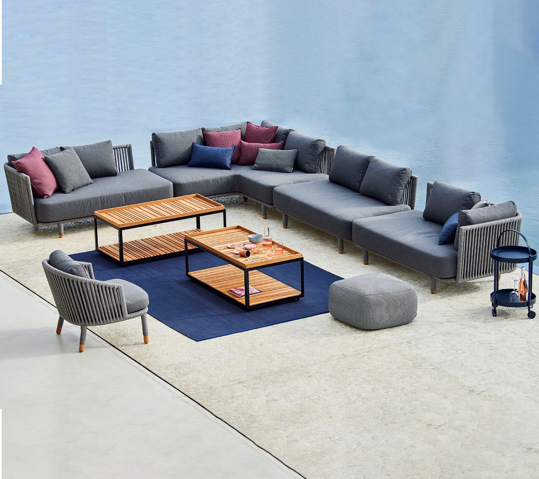 Zeitgemäße Sitzanordnung mit einem modularen grauen Sofa mit bunten Kissen, Couchtischen und einem passenden Akzentstuhl.