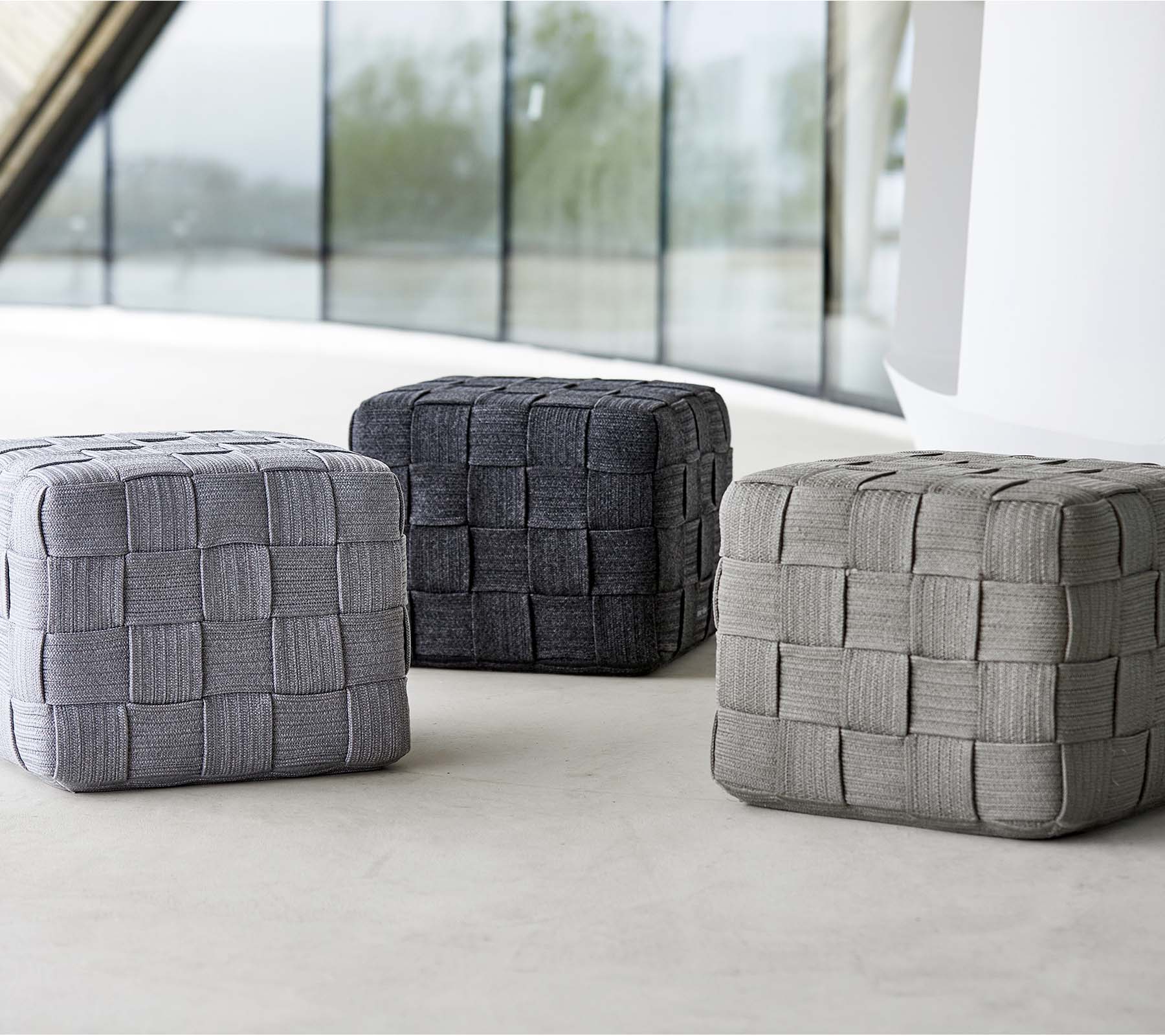 Drei gewebte Poufs in unterschiedlichen Grautönen mit einem strukturierten Design, auf einer hellen Oberfläche angeordnet. Ideal für Sitzgelegenheiten oder Dekoration.