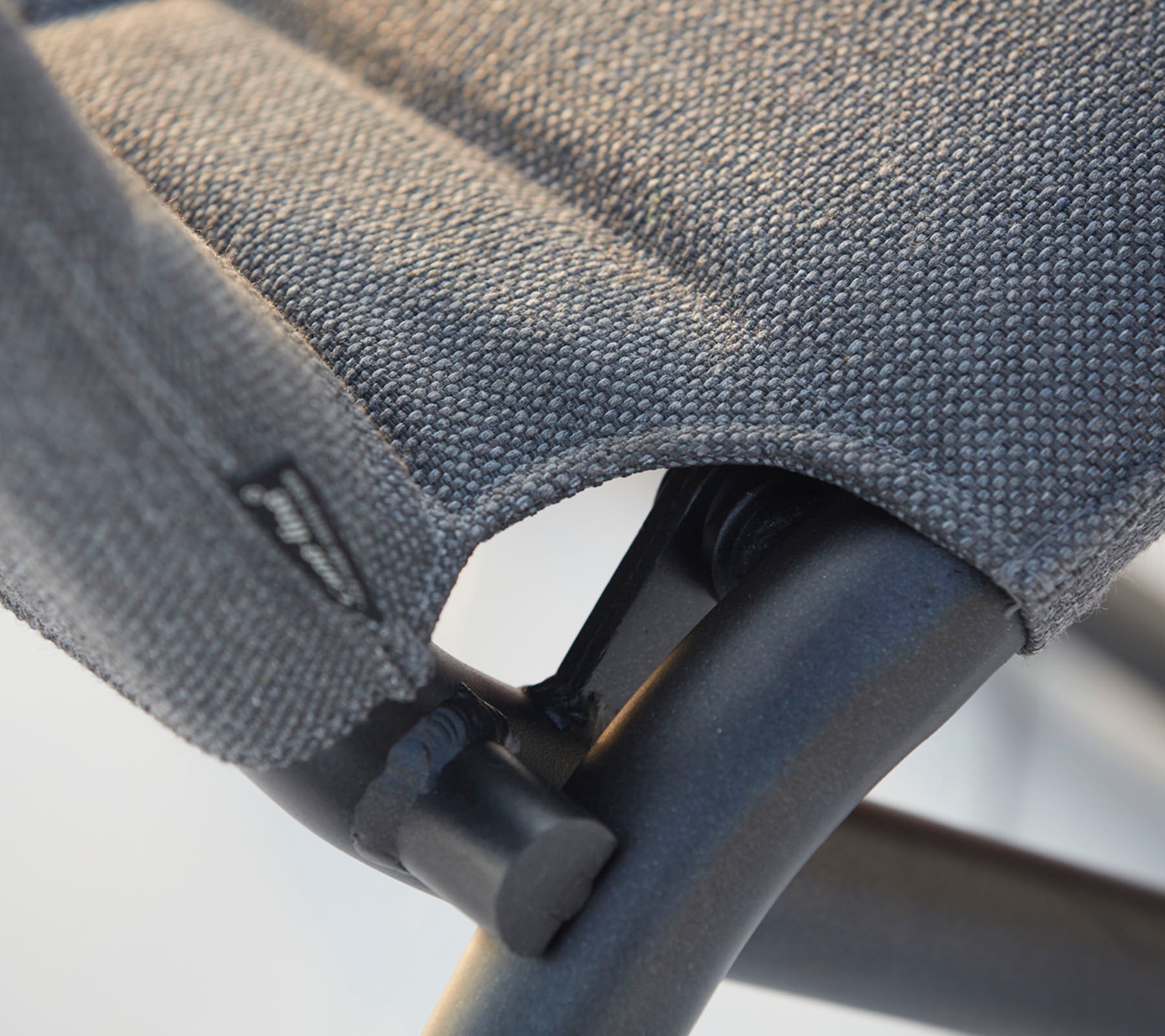 Nahaufnahme eines Stuhls mit strukturiertem Stoffbezug und stabilem schwarzen Rahmen, der die Nähte und Designdetails hervorhebt.