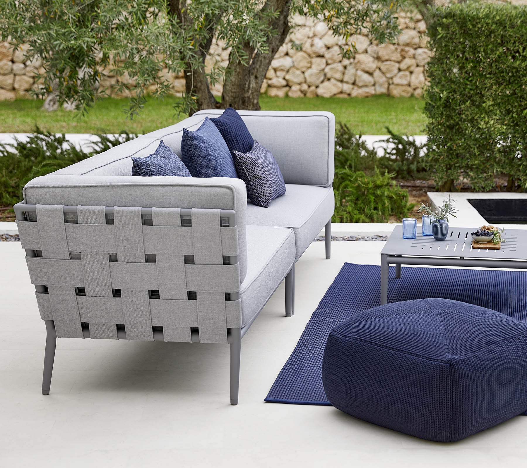 Moderne Außensitzgruppe mit einem grauen Sofa mit dekorativen Kissen, einem stilvollen Couchtisch und einem gemütlichen Pouf.