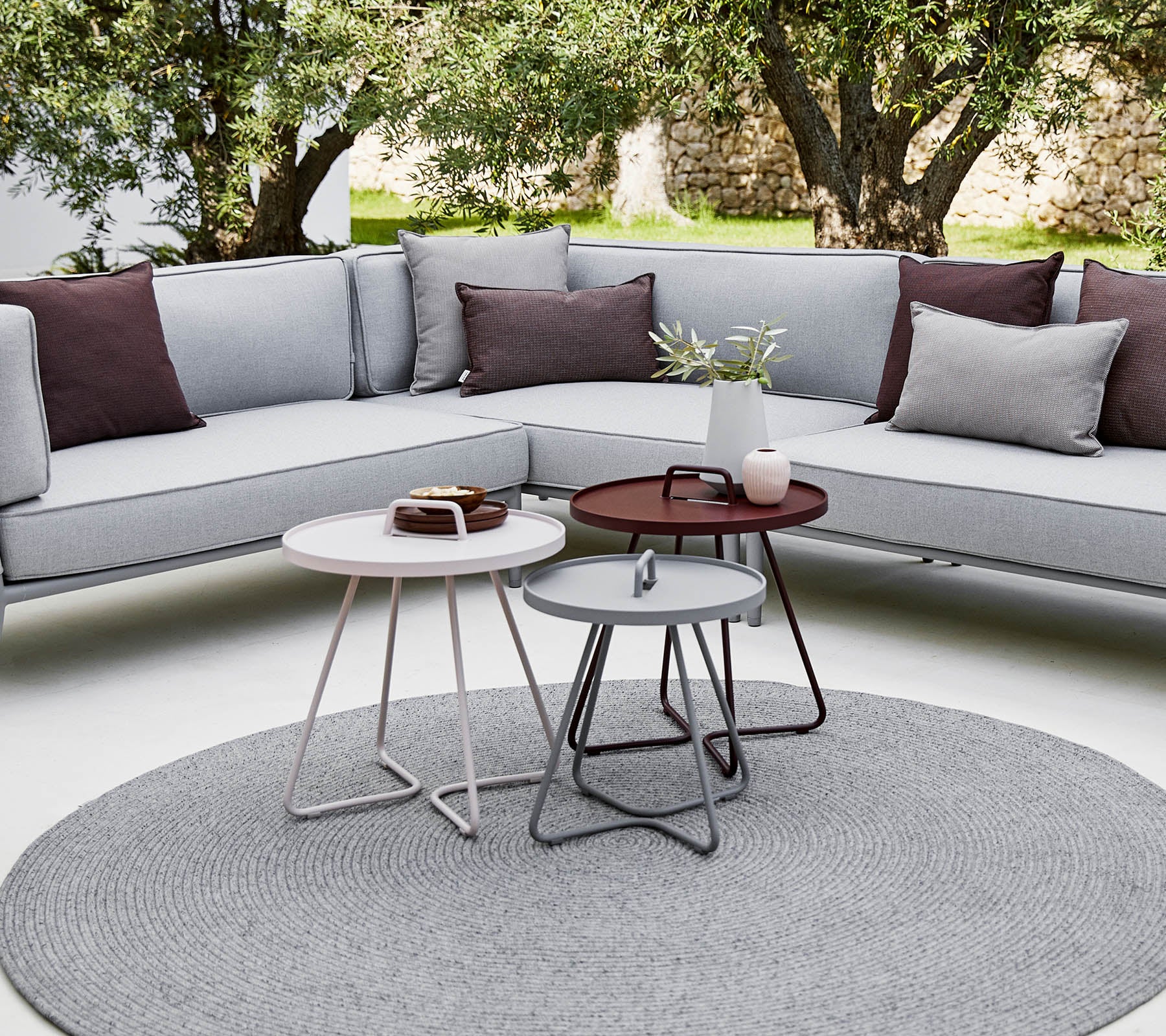Stylischer Außenbereich mit einer Ecksofa mit Kissen und modernen runden Kaffeetischen in einer entspannten, zeitgenössischen Umgebung.