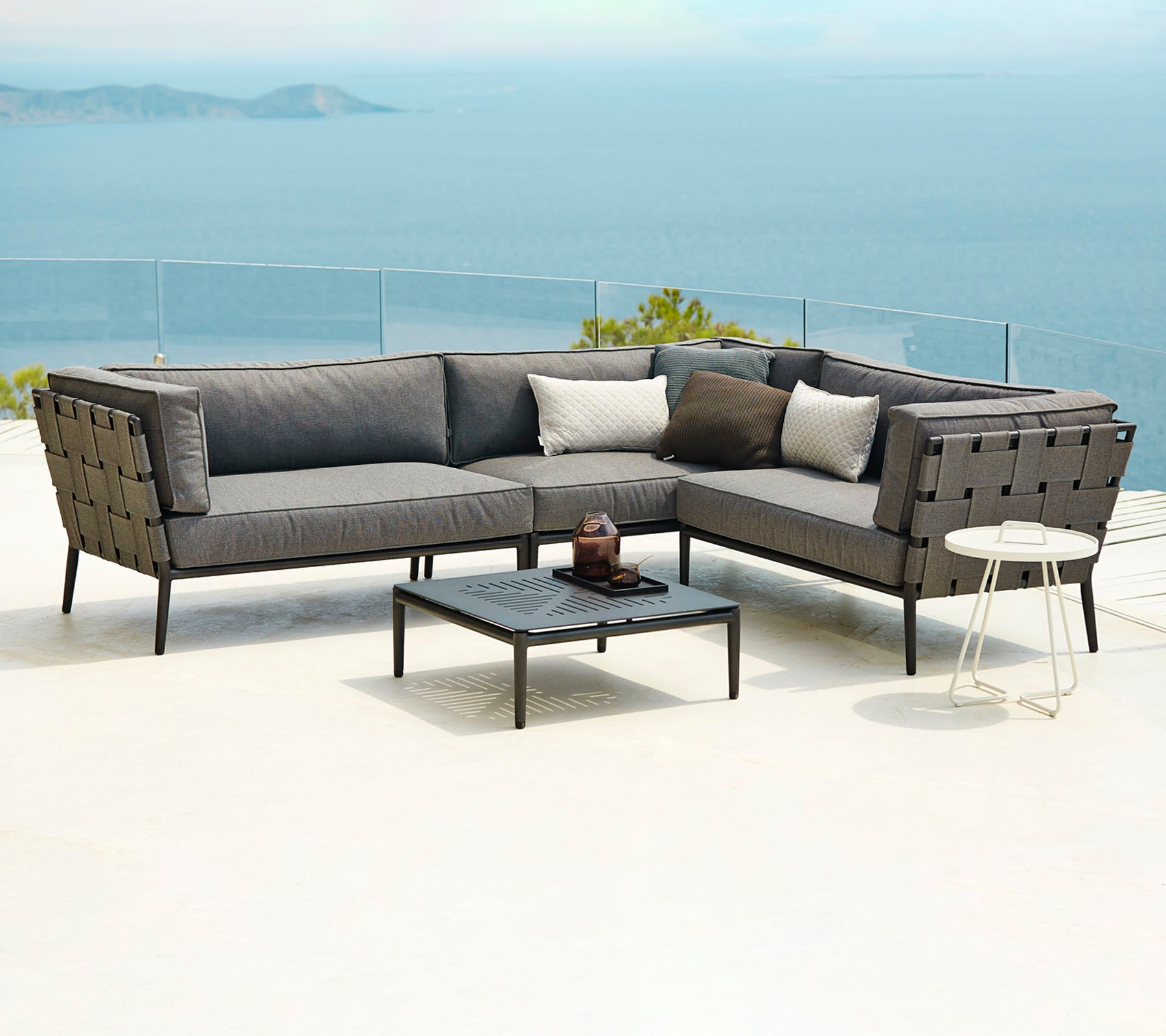 Moderne Außen Sitzanlage mit einer modularen Sofa mit Kissen und einem Couchtisch, vor einer malerischen Kulisse mit Wasser.