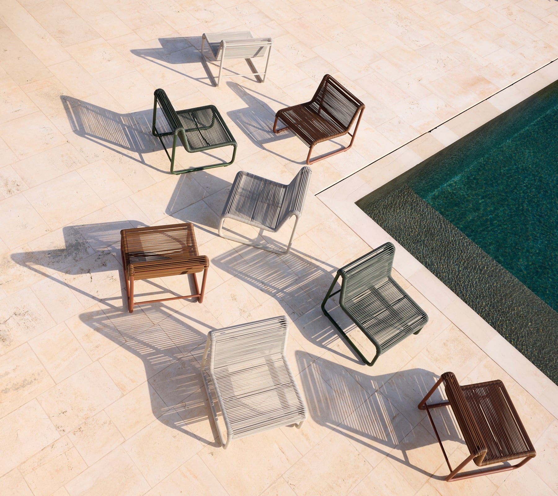 Verschiedene moderne Stühle in Braun, Grau, Weiß und Schwarz, die um einen Pool angeordnet sind.