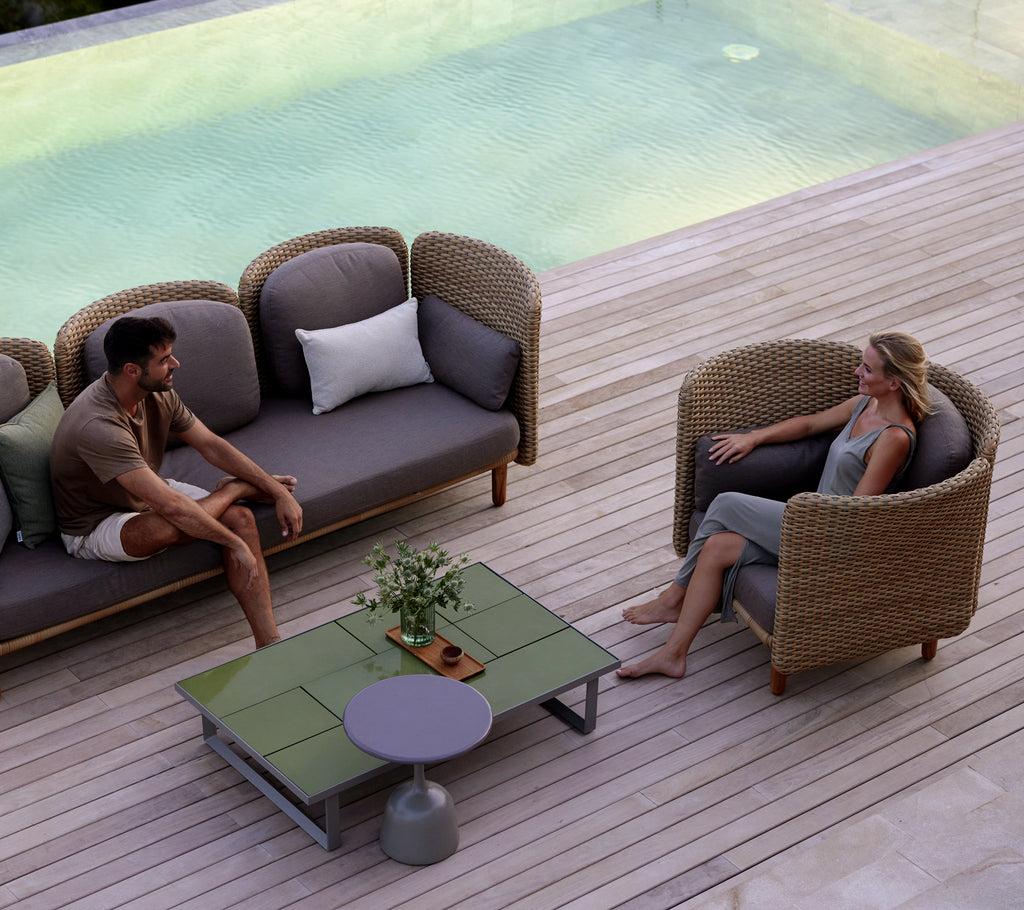 Zwei Personen sitzen in bequemen Loungestühlen um einen stylischen Couchtisch, mit einem ruhigen Wasserfall im Hintergrund.