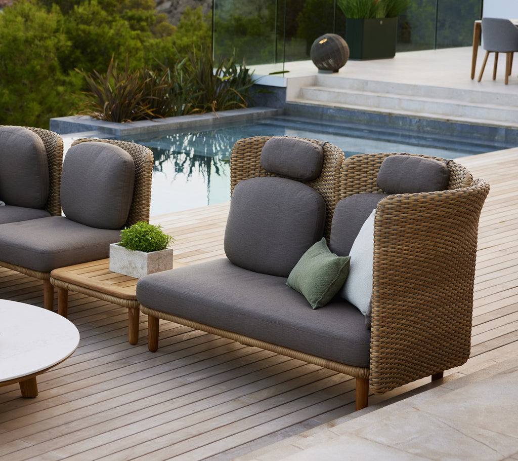 Stylische Couch mit hoher Rückenlehne und geschwungenen Armlehnen, ausgestattet mit grauen Kissen und einer Mischung aus dekorativen Kissen auf einem Holzdeck.