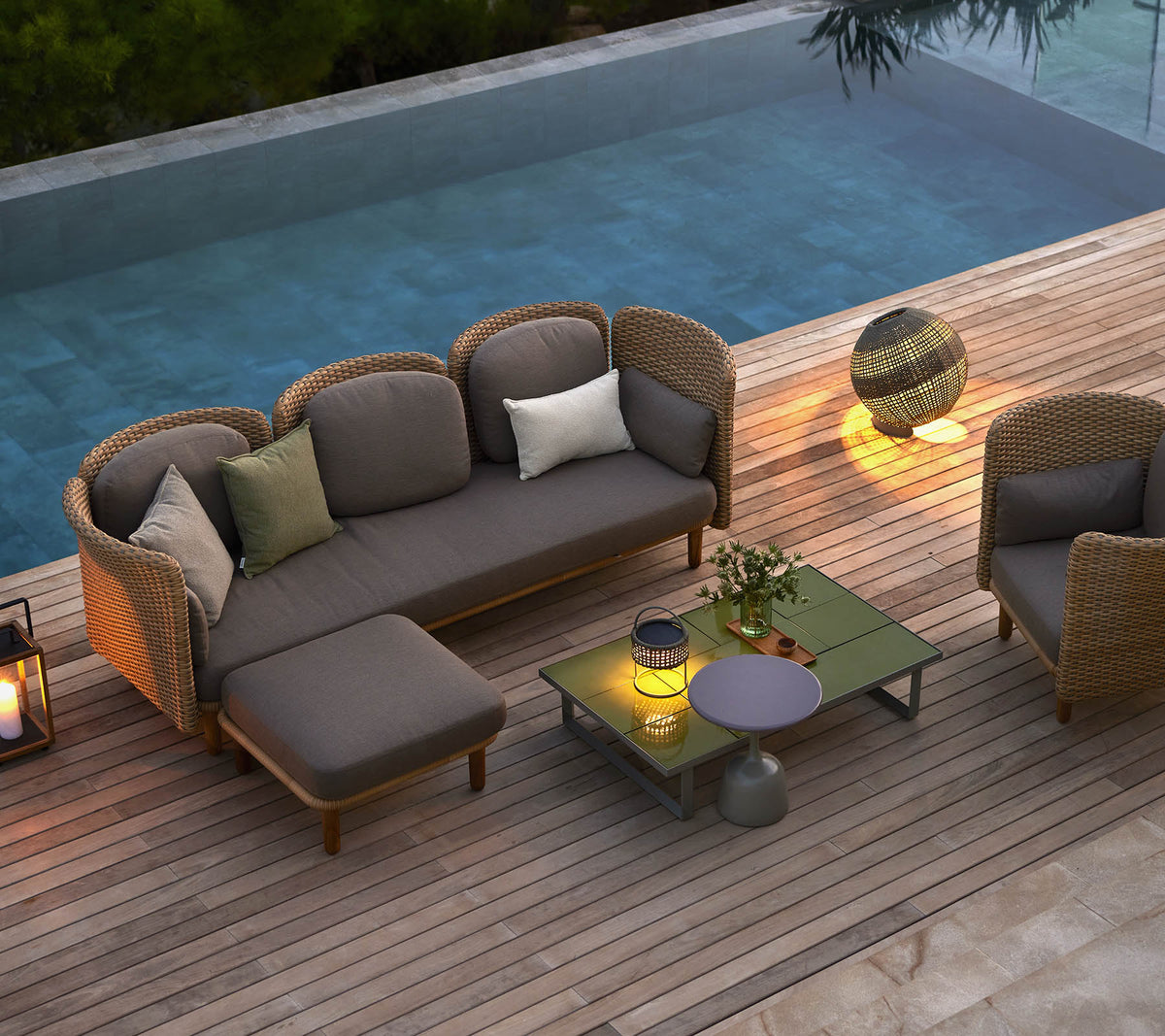 Stilvolle Loungemöbel mit Kissen, einem Couchtisch und ambienter Beleuchtung, neben einem ruhigen Pool.