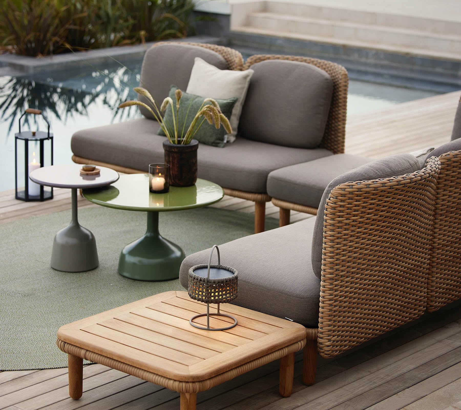 Ein stilvoller Loungebereich mit einem grauen Sofa mit Korbdetails, einem grünen Beistelltisch und dekorativen Accessoires.