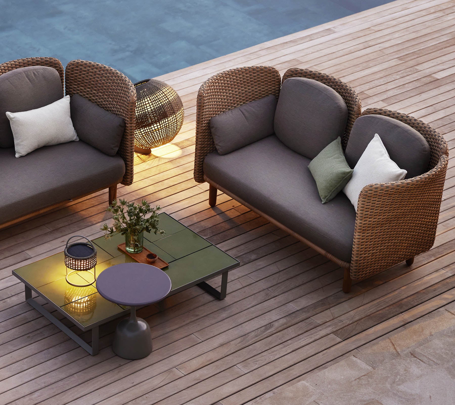 Ein gemütlicher Sitzbereich mit zwei geschwungenen Loungesofas, einem niedrigen Tisch, dekorativen Kissen und stimmungsvollem Licht.