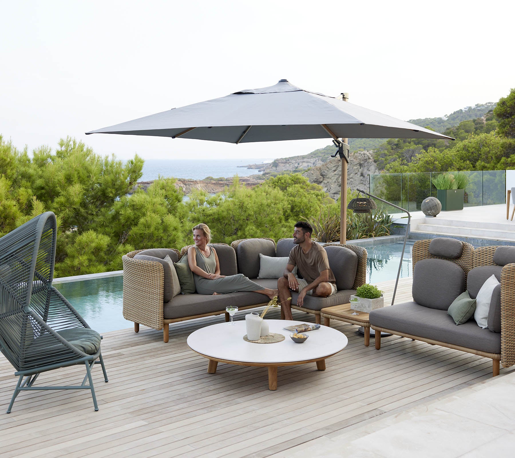 Ein stilvolles Lounge-Bereich mit bequemen Sitzgelegenheiten, einem großen Sonnenschirm und einem runden Tisch, umgeben von Grün und einer ruhigen Aussicht.
