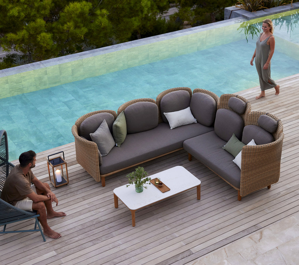 Ein modernes Bogensofa mit plüschigen Kissen und einem weißen Couchtisch, umgeben von Grünpflanzen und einem ruhigen Wassermerkmal.