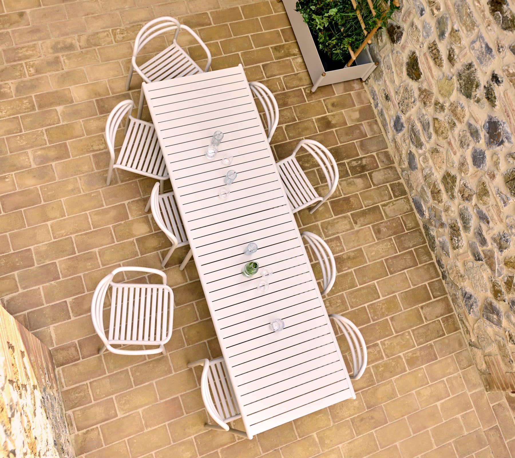 Luftaufnahme eines sandfarbenen Esstisches im Freien mit acht Bliss-Stühlen, der auf einer steinernen Terrasse steht.