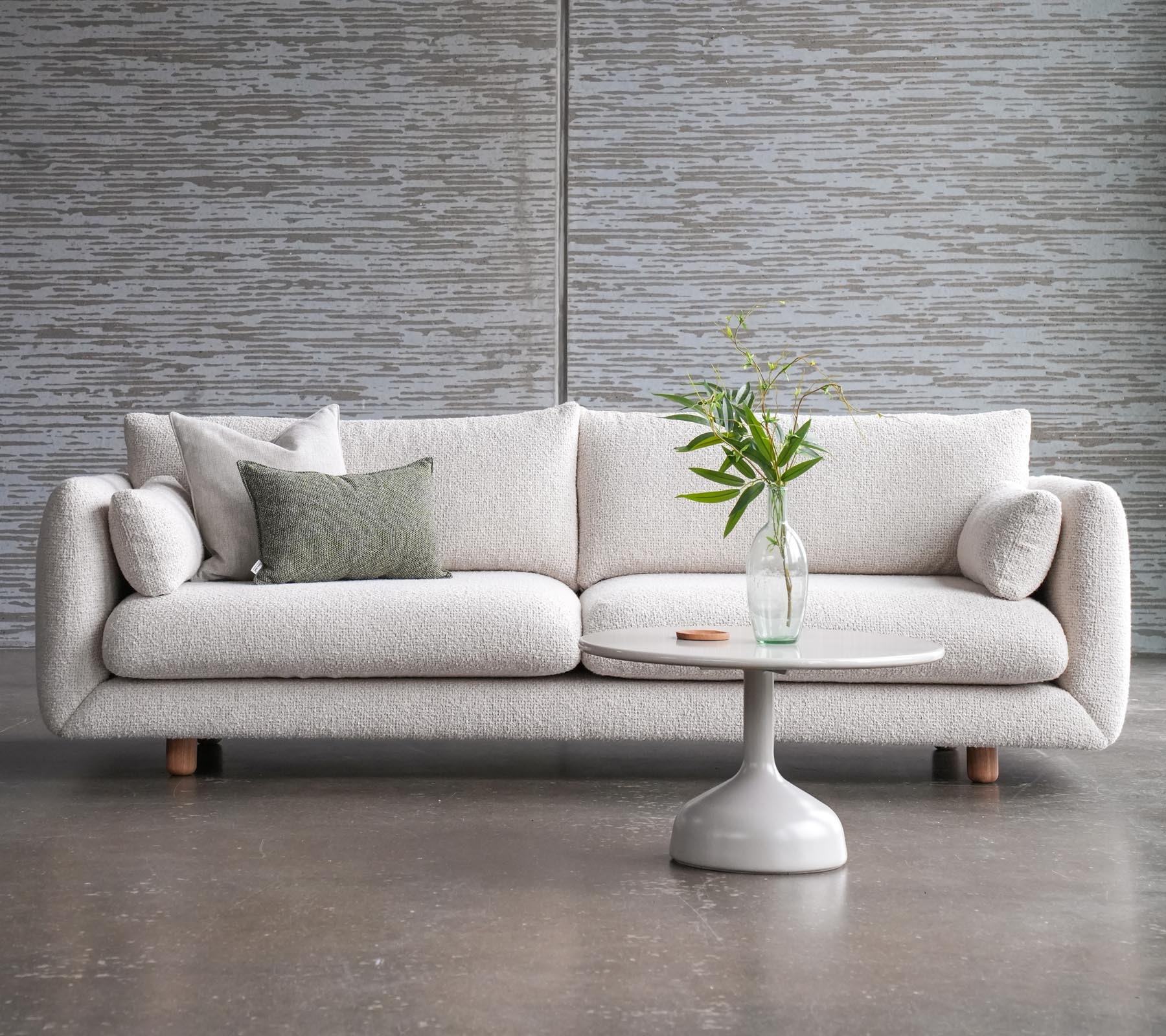 Ein stilvolles Sofa mit Kissen neben einem Glaxe-Couchtisch mit rundem Tischplatte und eleganten Teakbeinen, geschmückt mit einer Vase voller Blumen.