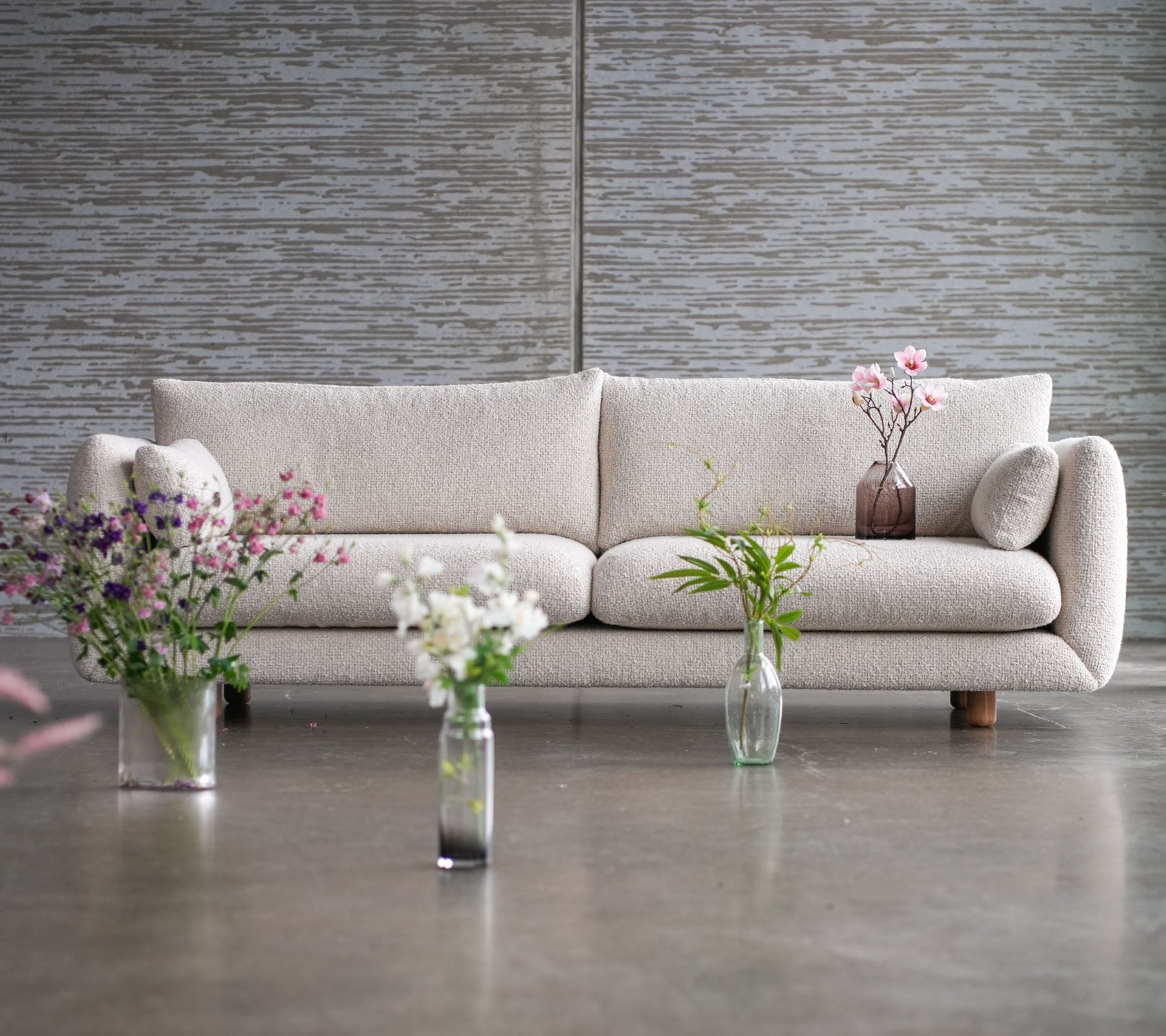 Ein hellfarbiges Sofa mit Teakbeinen, umgeben von Blumenvasen, die eine Mischung aus Eleganz und Cane-line Flair zeigen.