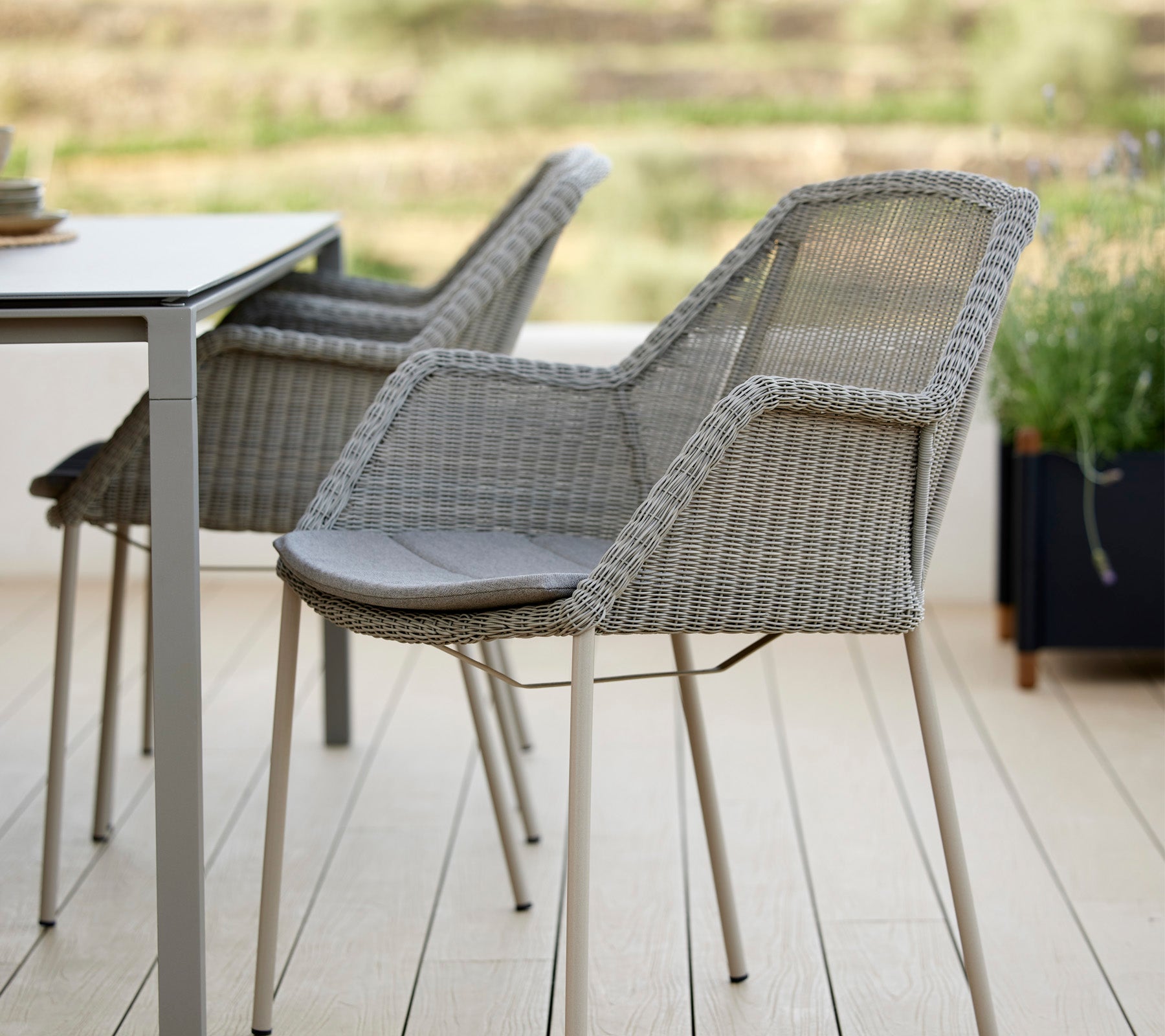 Zwei stilvolle geflochtene Stühle neben einem modernen Tisch mit elegantem Design und bequemen Kissen, ideal zur Entspannung in einer ruhigen Umgebung.