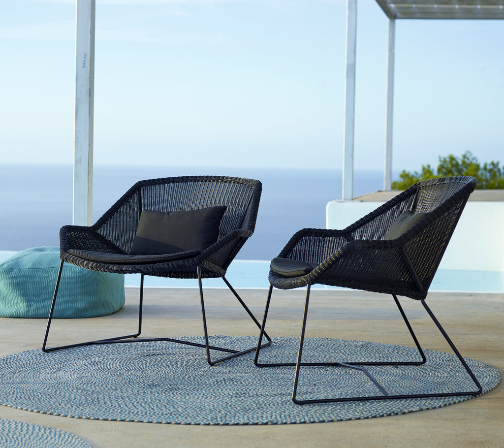 Zwei moderne schwarze Stühle mit einem blauen Kissen auf einem runden Teppich am Pool.