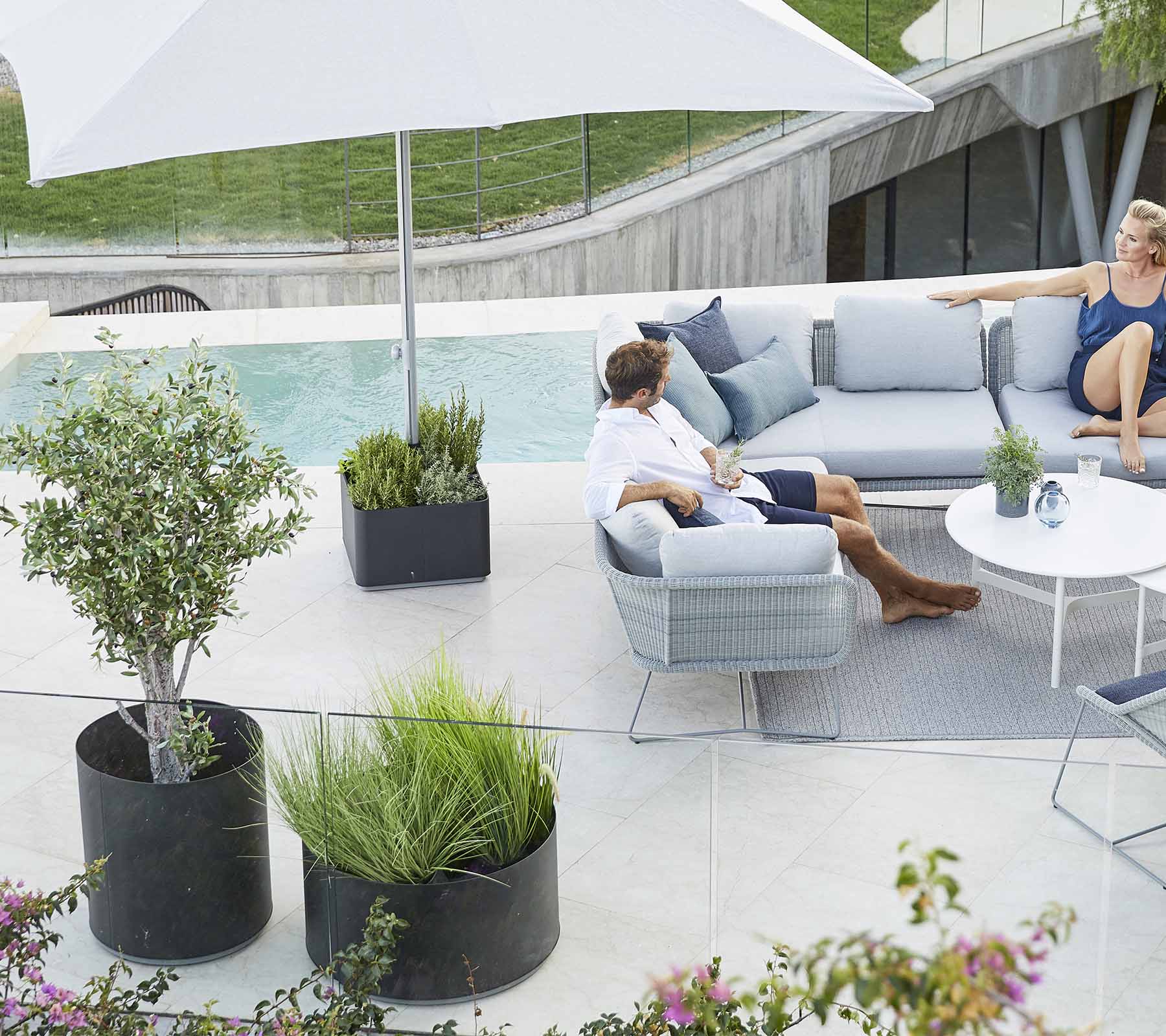 Ein stilvoller Außenbereich mit einer bequemen Couch, Pflanzen und einem großen Sonnenschirm, perfekt zum Entspannen.