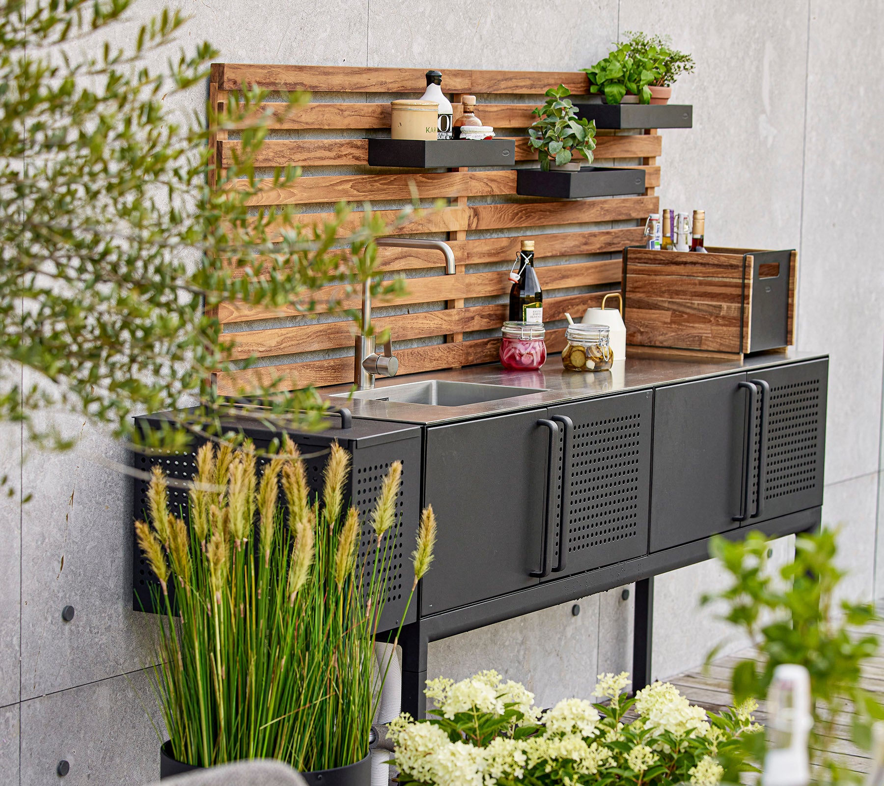 Moderne schwarze Kücheneinheit mit einem Waschbecken, Holzregalen und verschiedenen Pflanzen, die einen stilvollen und funktionalen Arbeitsplatz schaffen.