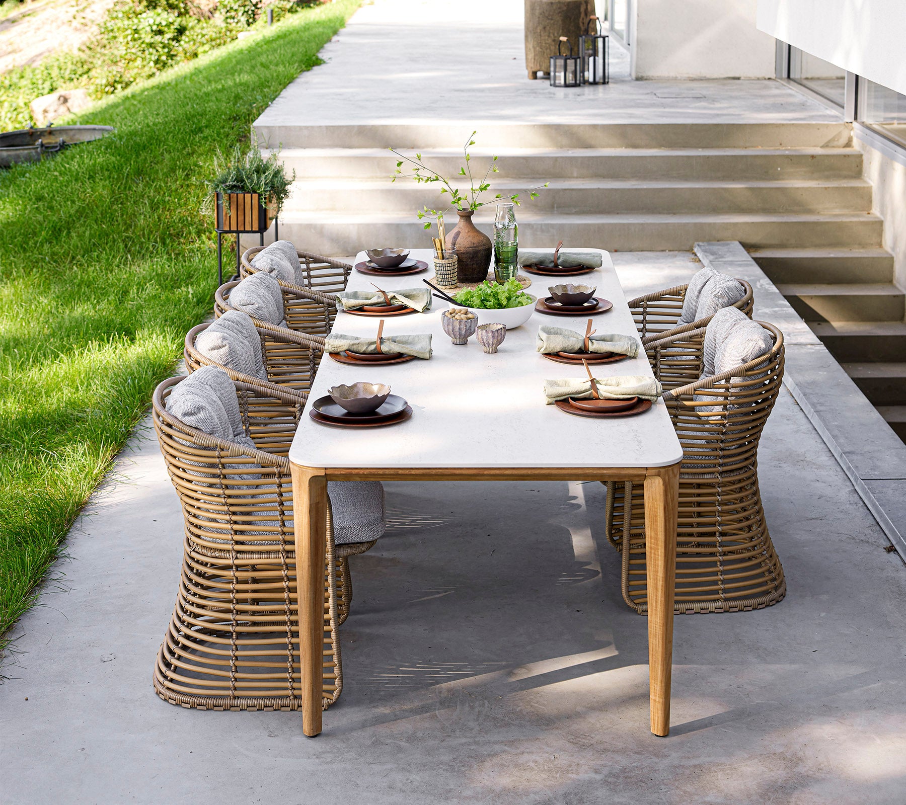 Ein stilvolles Esszimmer-Set mit elegantem Geschirr und bequemen Stühlen, umgeben von Grün und natürlichem Licht. Perfekt für Zusammenkünfte.
