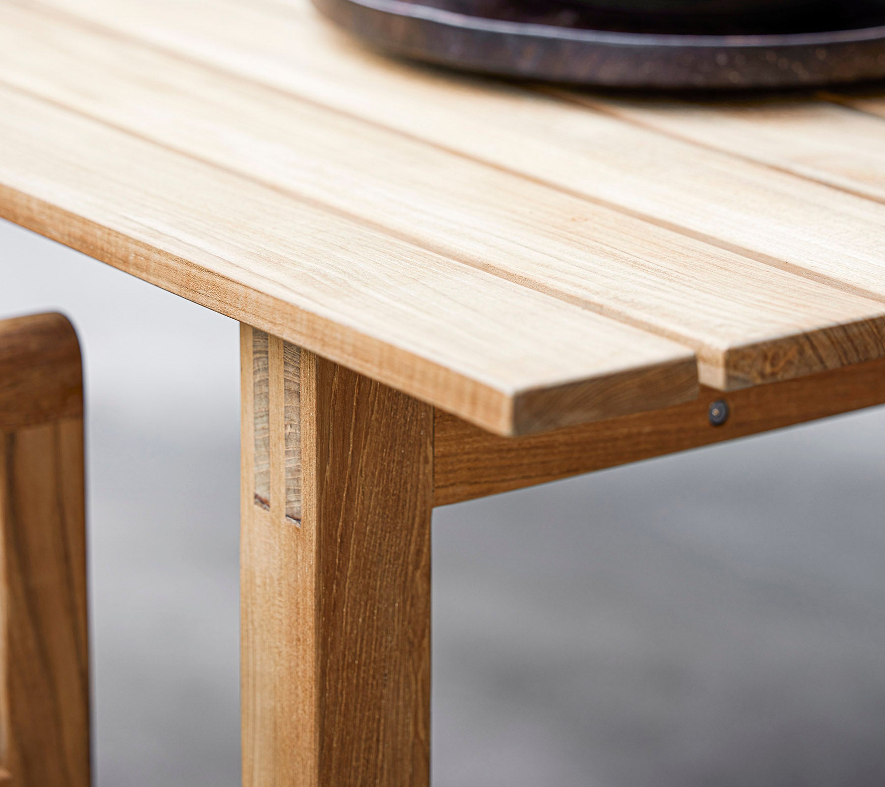 Nahaufnahme eines Holztisches mit Lamellen-Design und einer dunklen runden dekorativen Schale darauf. Perfekt für moderne Essästhetik.