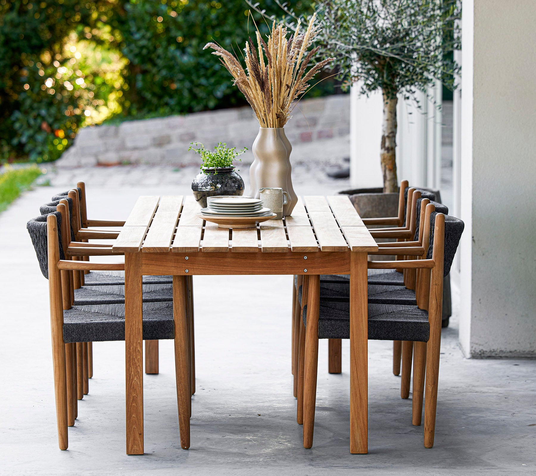 Ein Holztisch, umgeben von acht stilvollen Stühlen, dekoriert mit einer Vase und Pflanzen, schafft einen einladenden Essbereich.