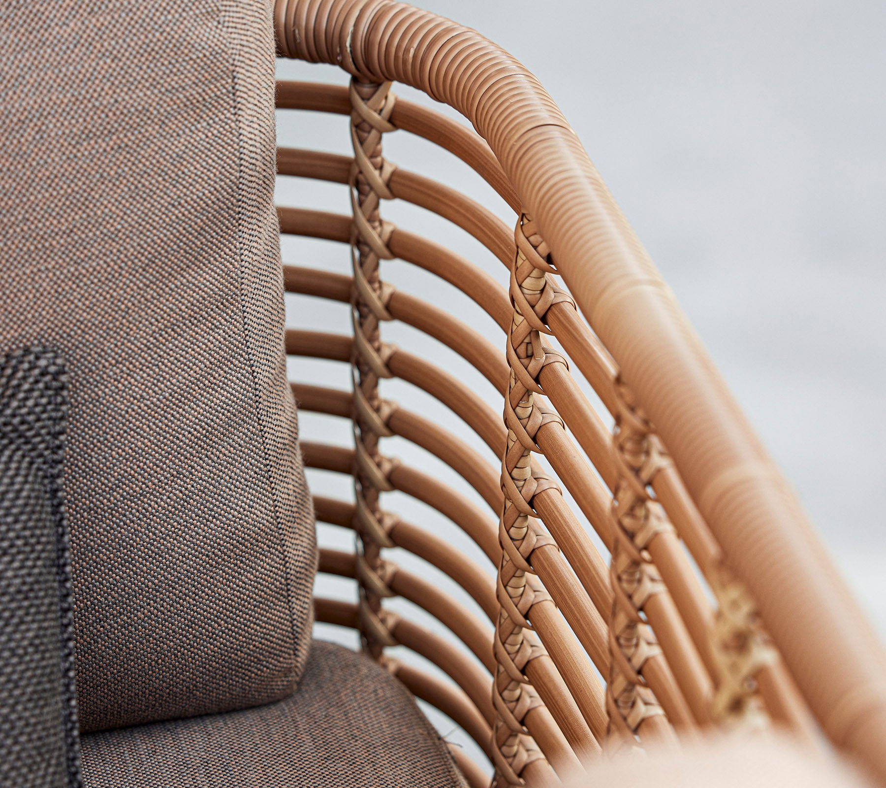 Nahaufnahme eines stilvollen Sessel mit geflochtenen Rattandetails und weichen Kissen in neutralen Tönen, die modernes Design zur Geltung bringen.