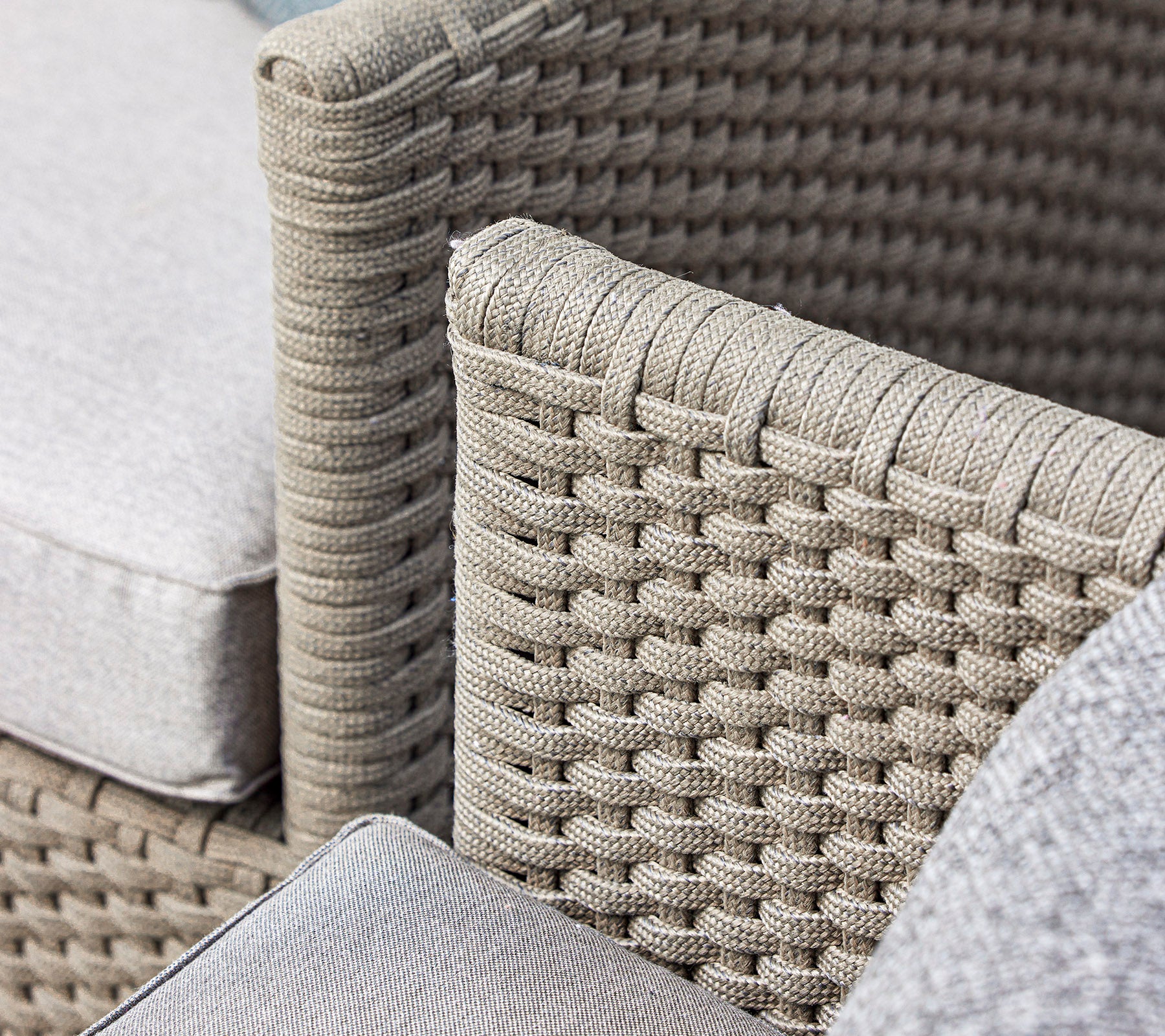 Nahaufnahme eines geflochtenen Korbstuhldesigns mit weichen Kissen in einem neutralen Farbton, das Handwerk und Textur präsentiert.