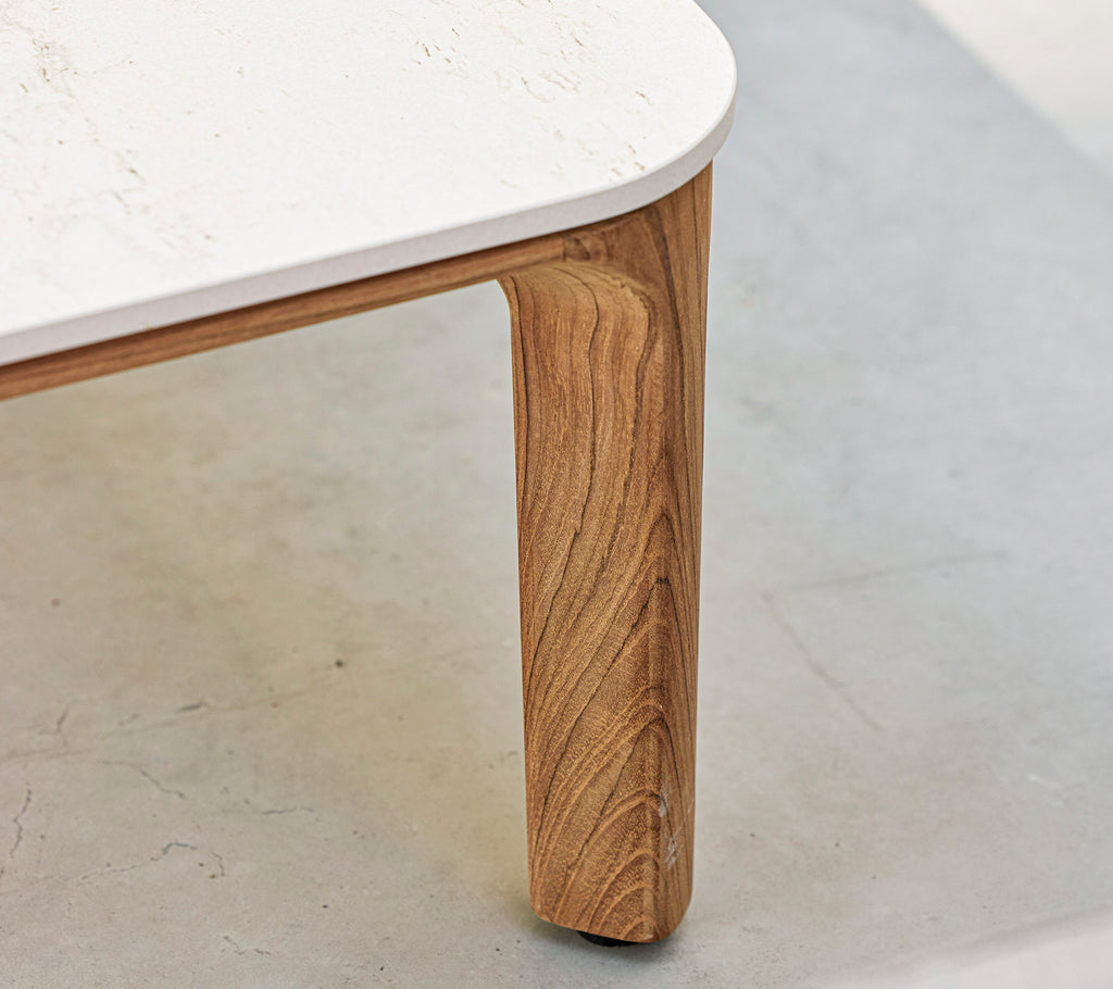 Eine Nahaufnahme eines Tisches mit einem strukturierten Holzbein und einer glatten, weißen Tischplatte. Elegante und moderne Designelemente werden hervorgehoben.