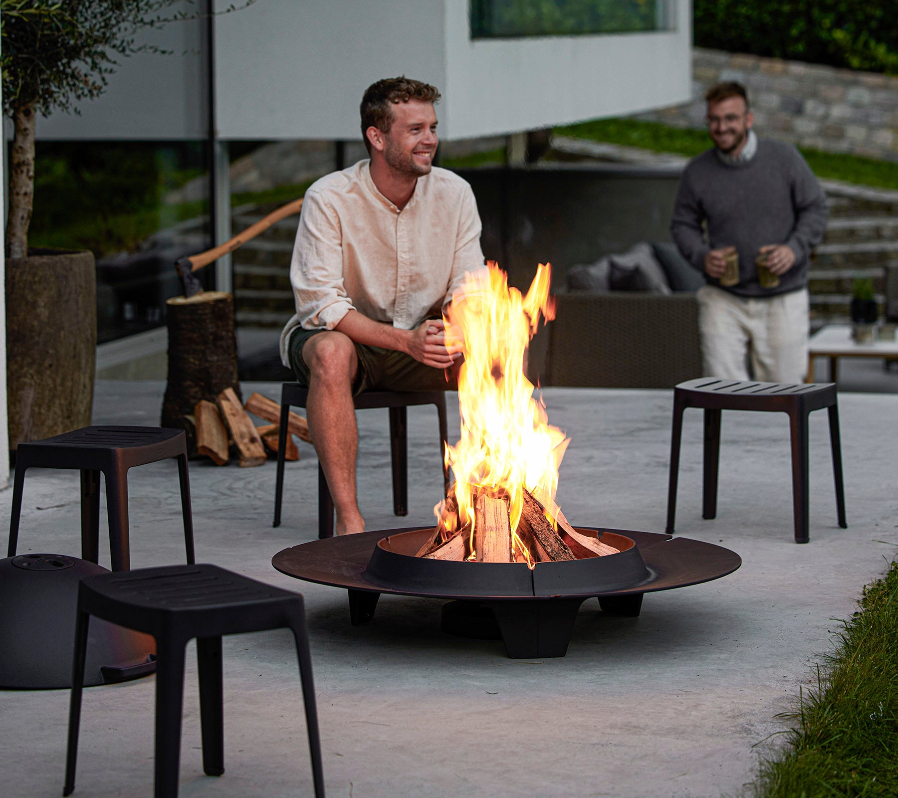 Zwei Männer genießen ein Feuerstelle, umgeben von modernen Sitzgelegenheiten, die eine gemütliche Atmosphäre für Entspannung und Gespräche schaffen.