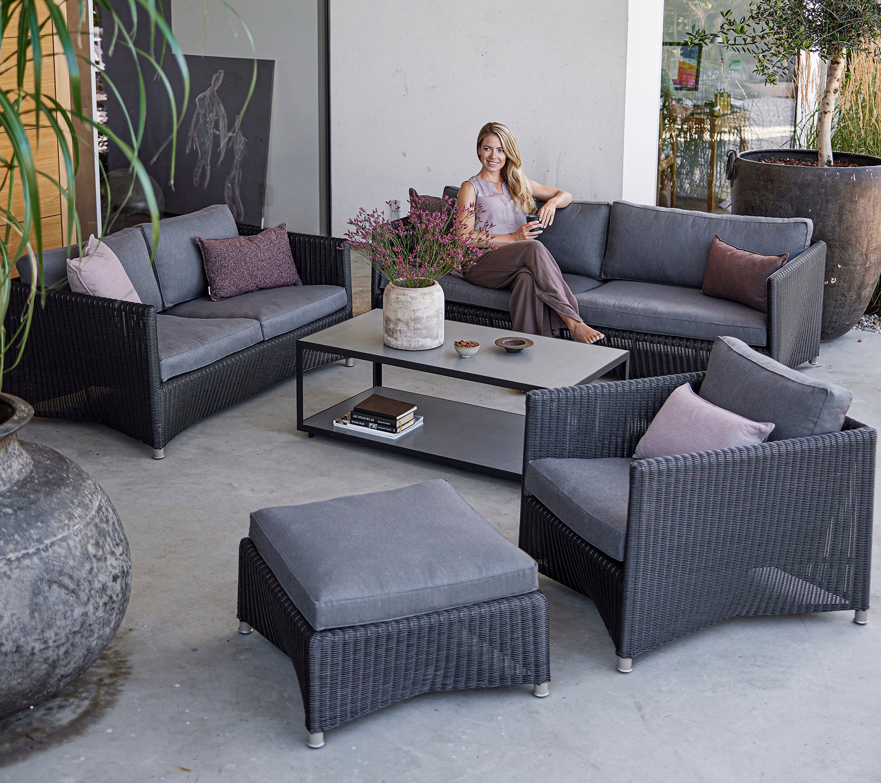 Eine moderne Sitzgelegenheit im Freien mit einer Frau, die sich auf einem stilvollen grauen Stoffsofa-Set mit Kissen und einem Couchtisch entspannt.