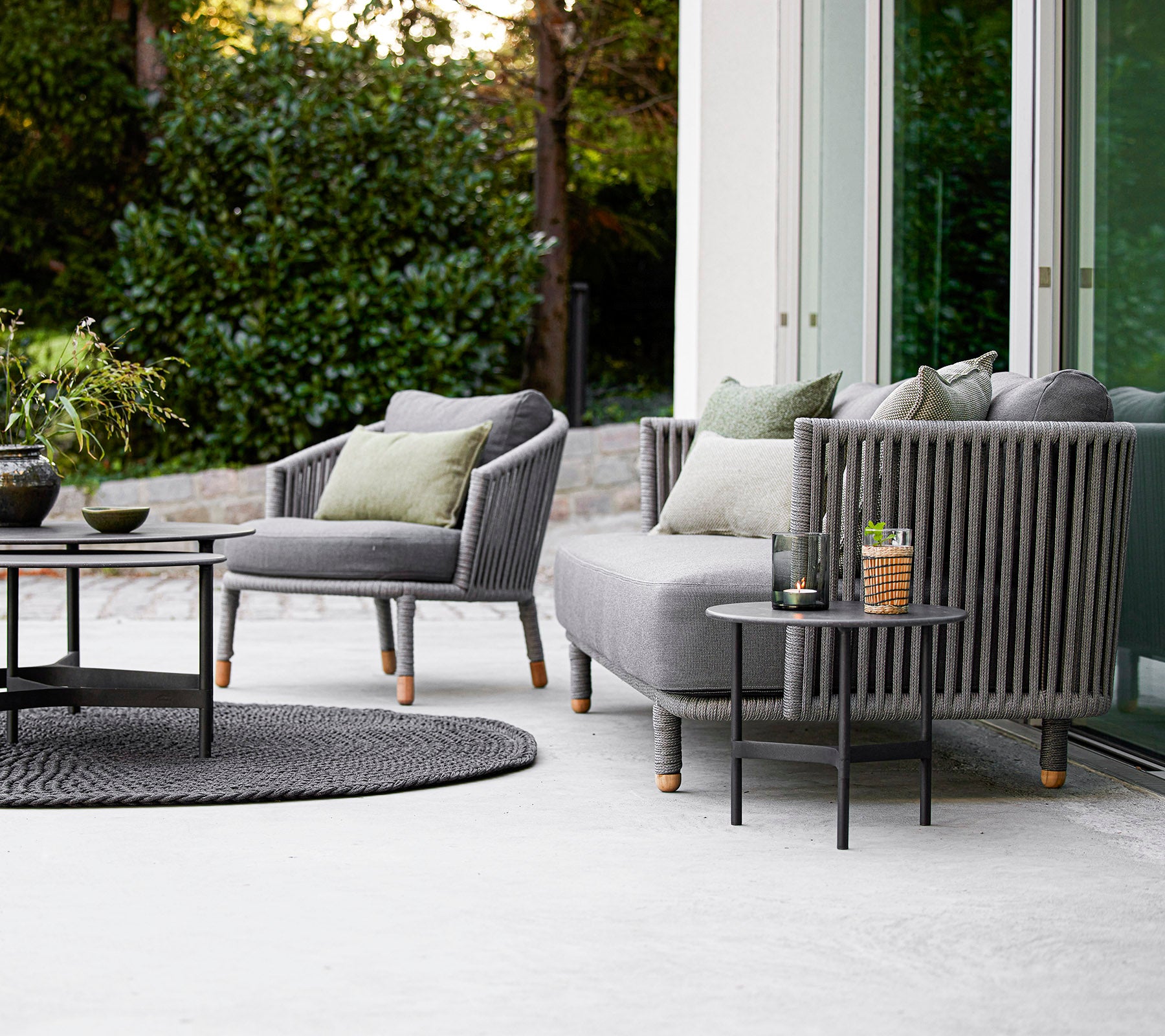 Zeitgemäßes Gartenset mit einem Sofa und Sessel mit Kissen, kombiniert mit einem runden Couchtisch und dekorativen Accessoires.