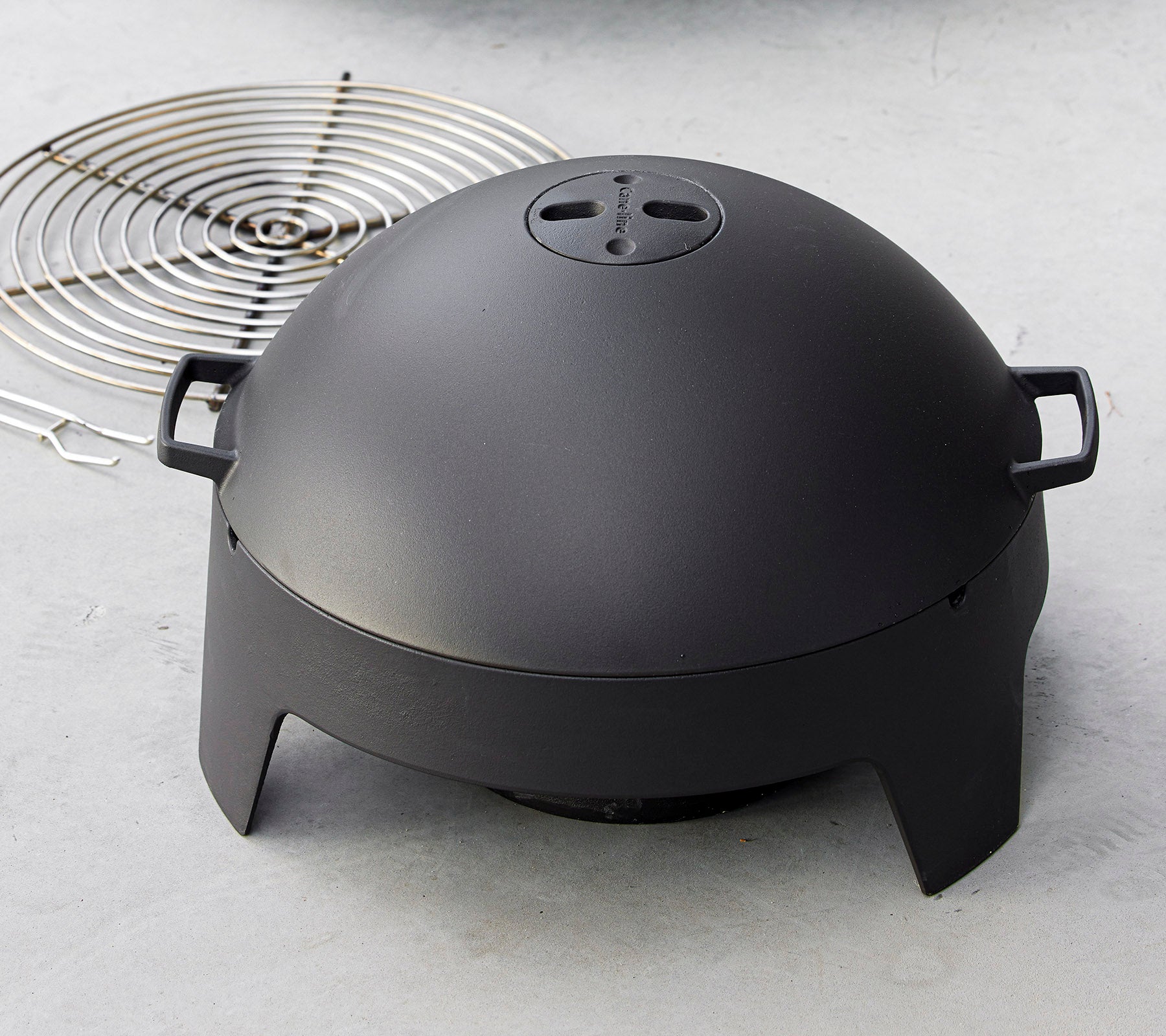 Ein elegantes schwarzes Kochgerät in Kuppelform mit Griffen, begleitet von einem runden Grillrost. Ideal zum Grillen und Kochen im Freien.