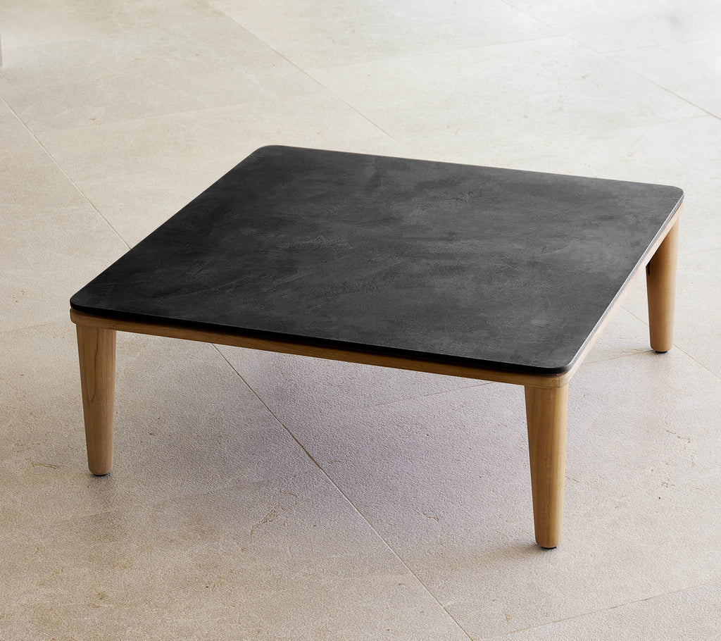 Quadratischer schwarzer Tisch mit Holzbeinen in einem minimalistischen Umfeld.