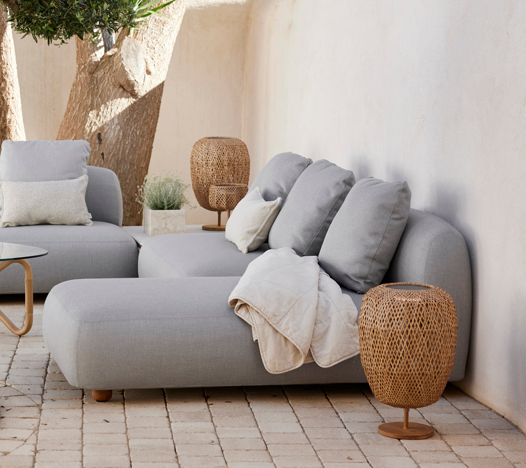 Modernes graues Sofa mit Kissen und einem geflochtenen Beistelltisch in einem minimalistischen Wohnzimmer.