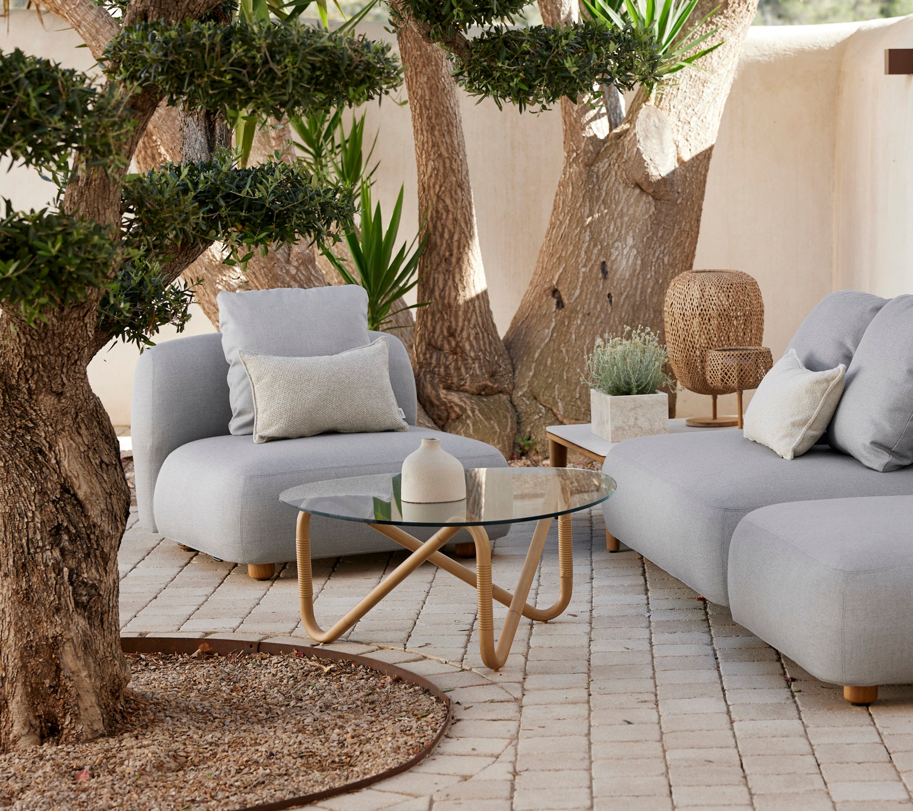 Moderne graues Sofa mit Kissen und einem Glastisch in einer entspannten Outdoor-Umgebung.