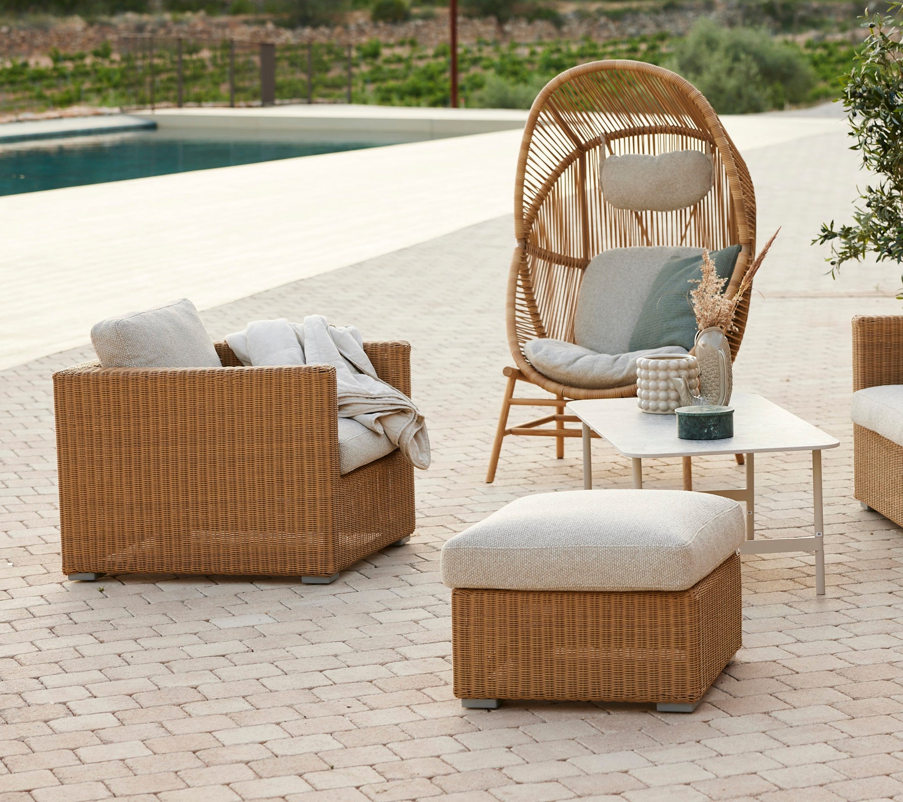 Moderne Lounge-Bereich mit einem Rattanstuhl, grauen Kissen, Rattan-Sofa und einem Couchtisch.