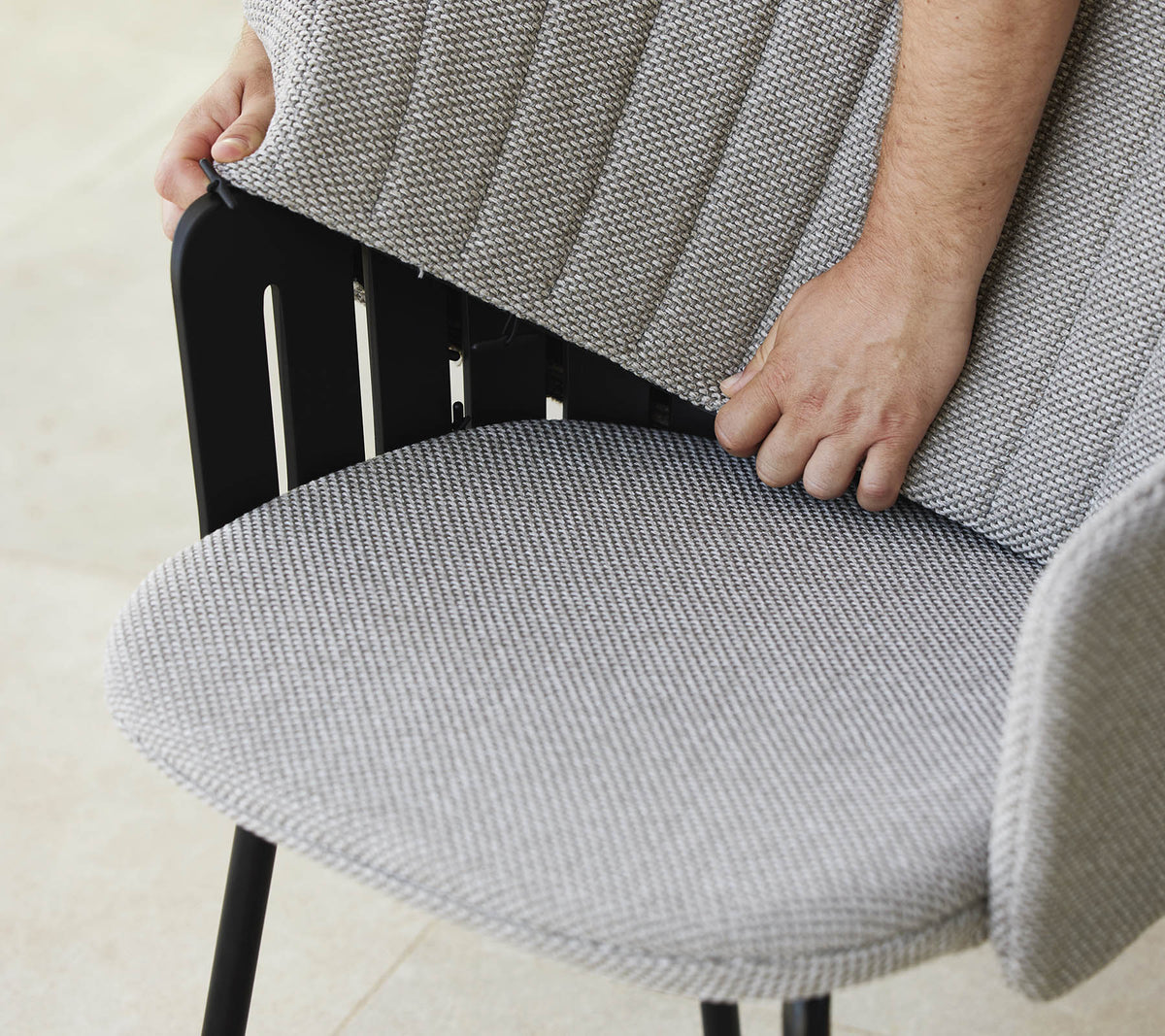 Person passt die Rückenlehne eines modernen Stuhls mit einem strukturierten Stoffsitz an, der ein stilvolles Design und ergonomische Unterstützung zeigt.